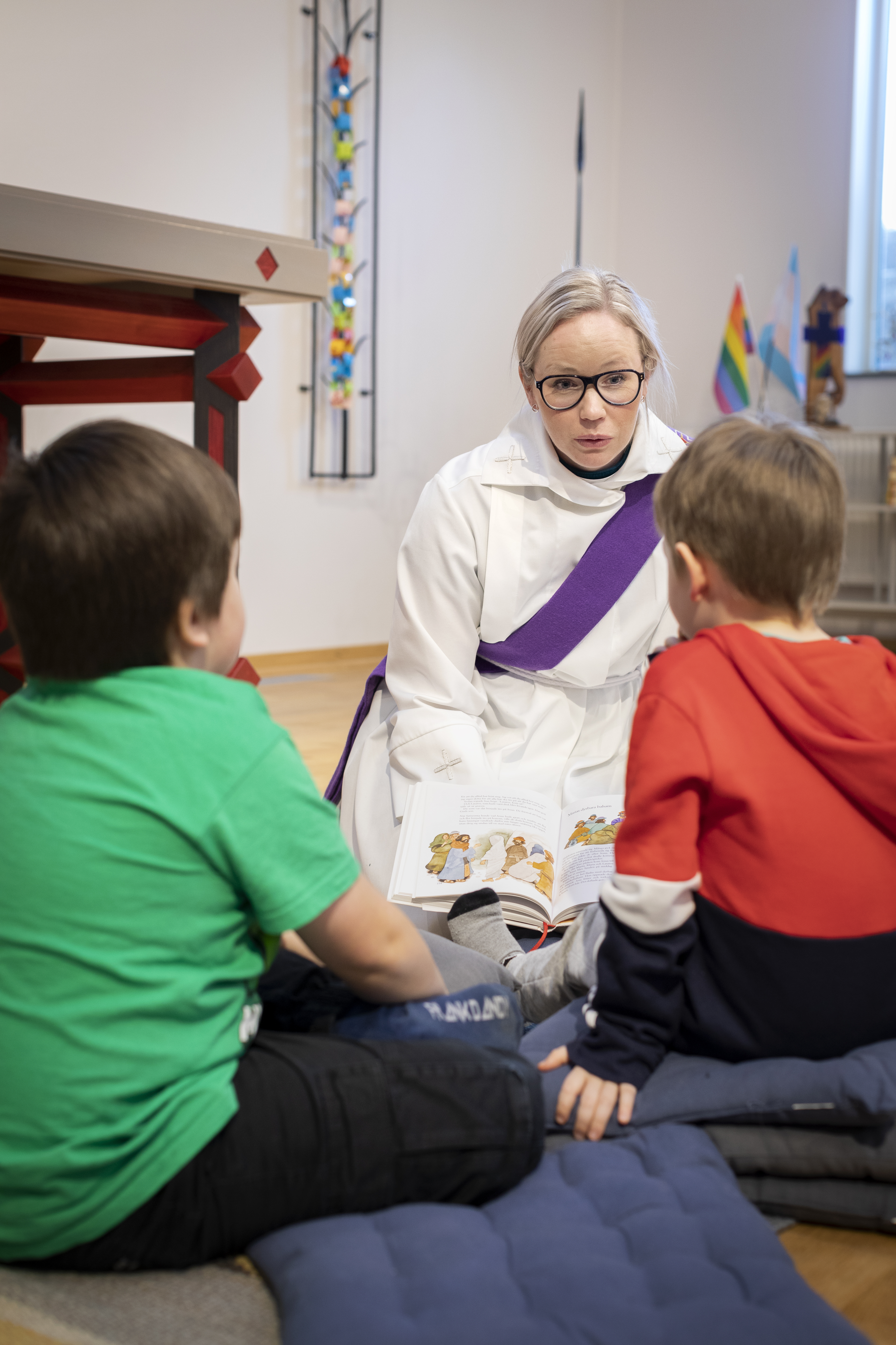 En kvinnlig diakon sitter på golvet med två barn.