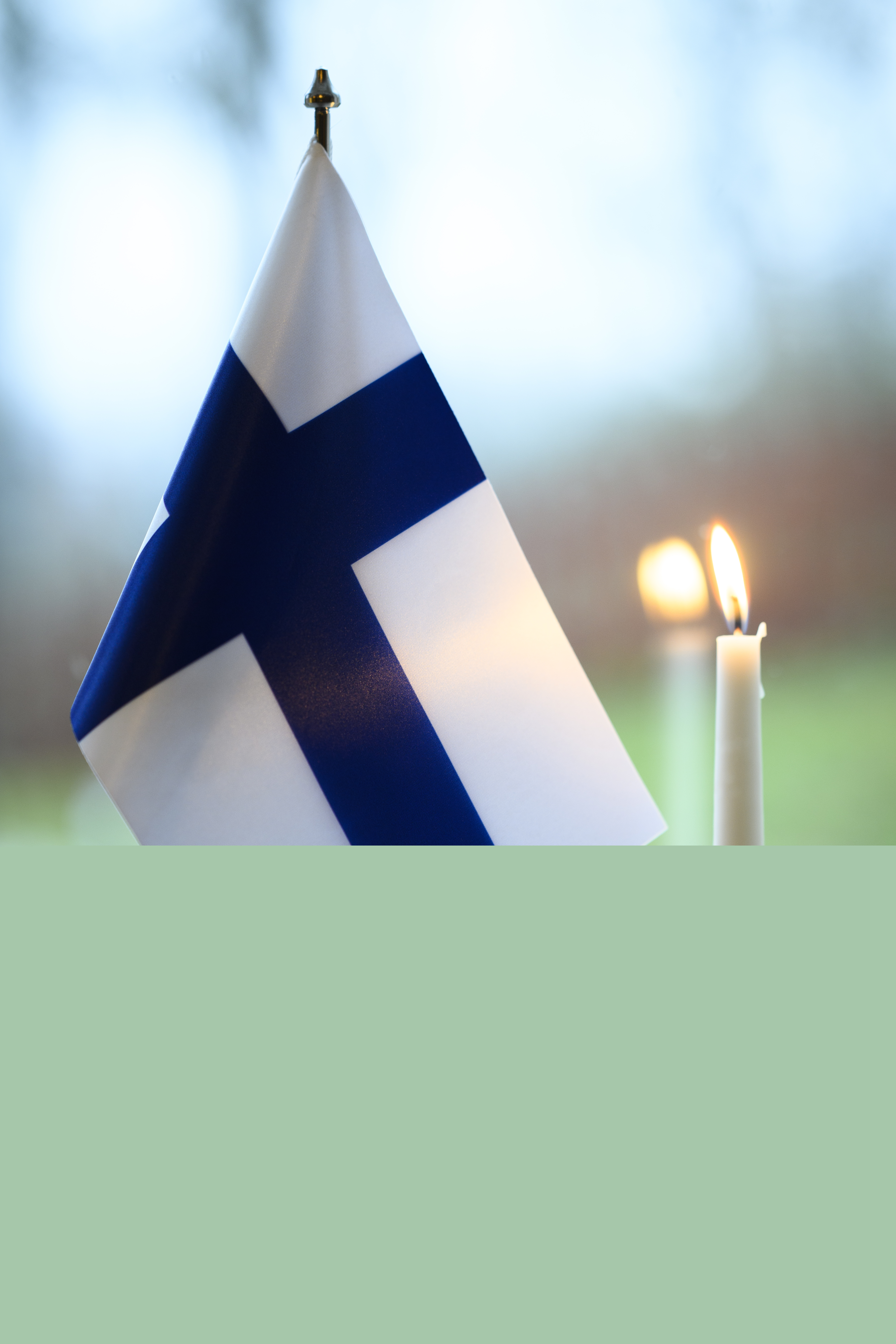 En finsk bordsflagga och ett brinnande stearinljus står i ett fönster.