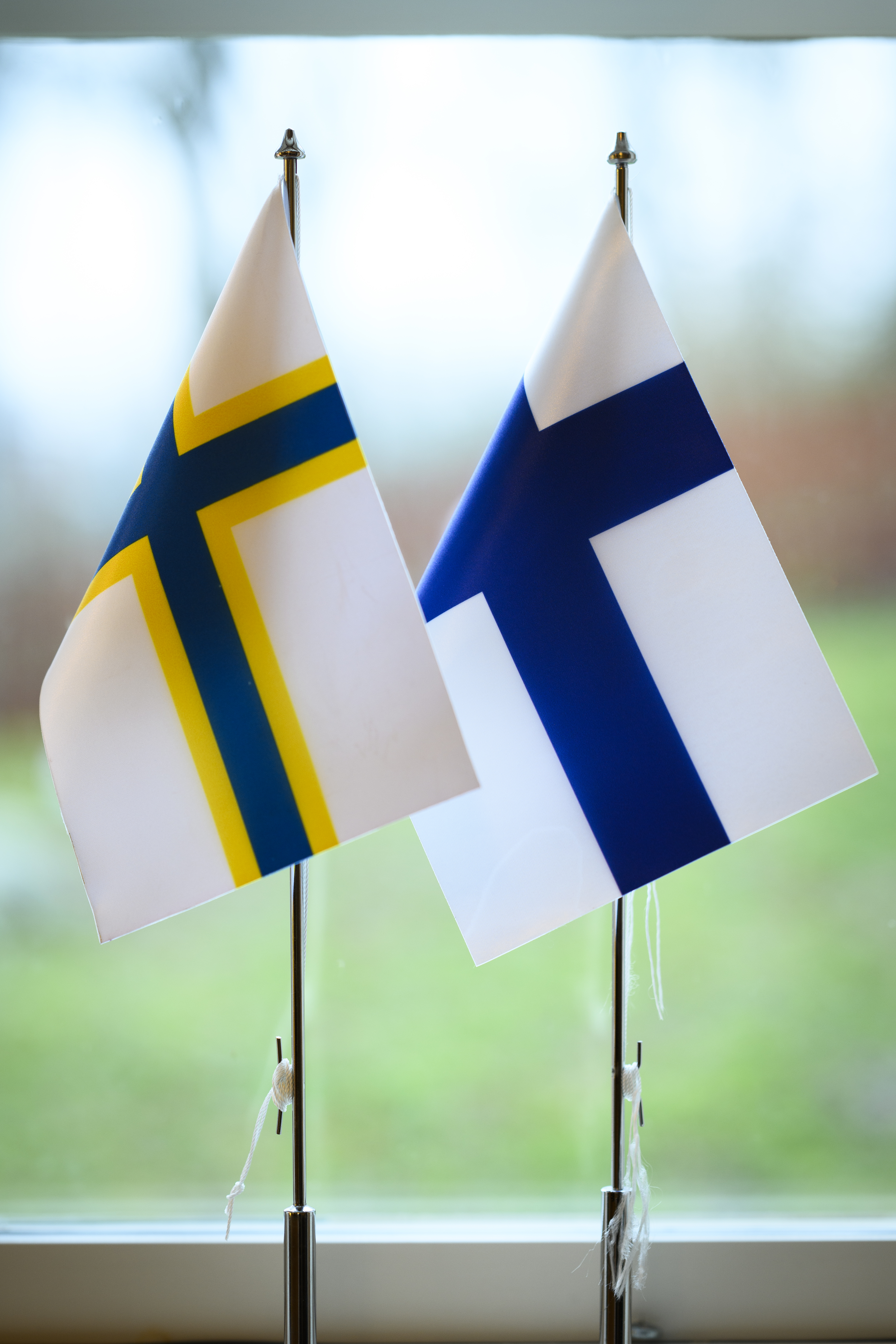 En finsk och en sverigefinsk bordsflagga står i ett fönster.