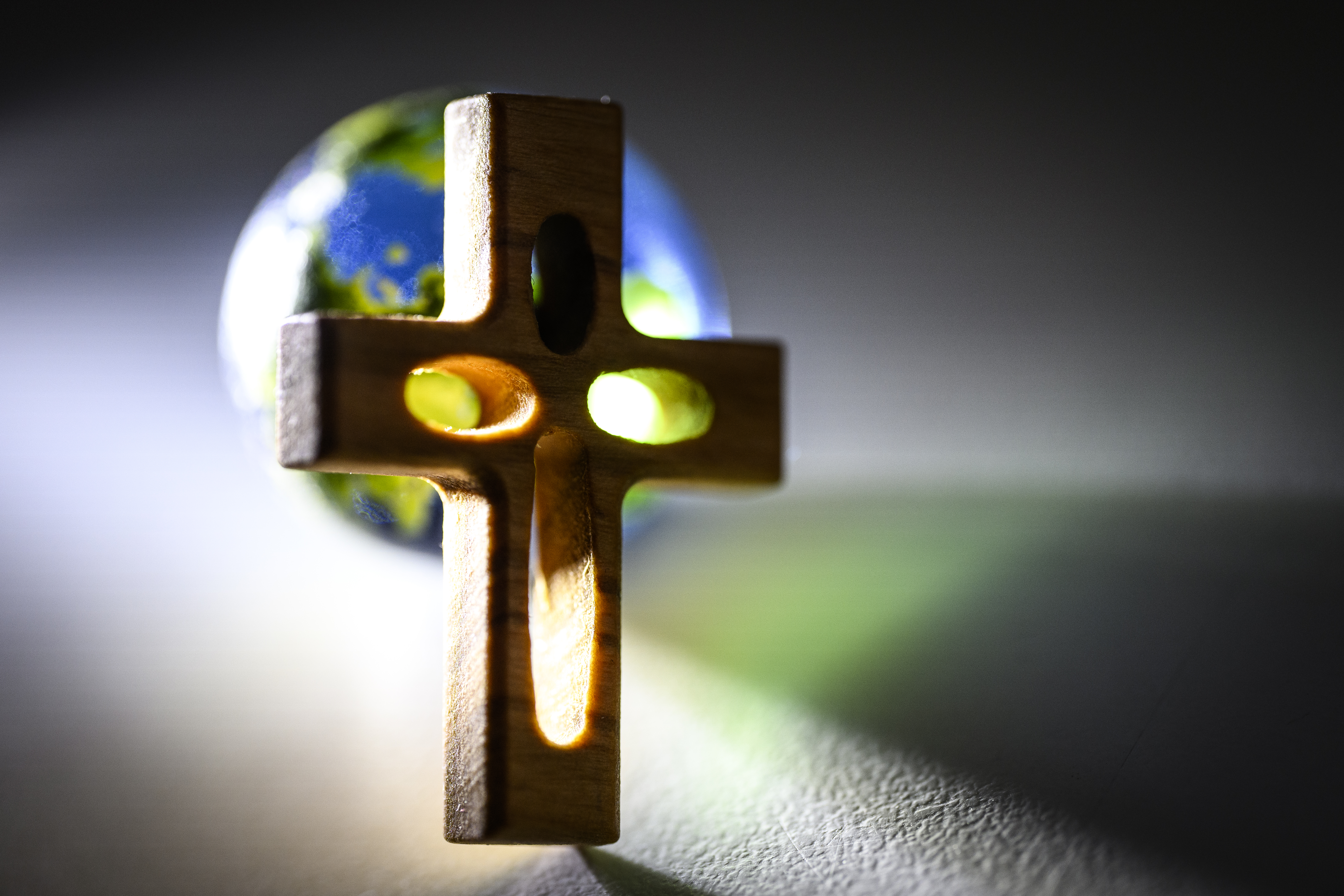 Solen lyser upp ett litet kors i trä. En jordglob i bakgrunden.