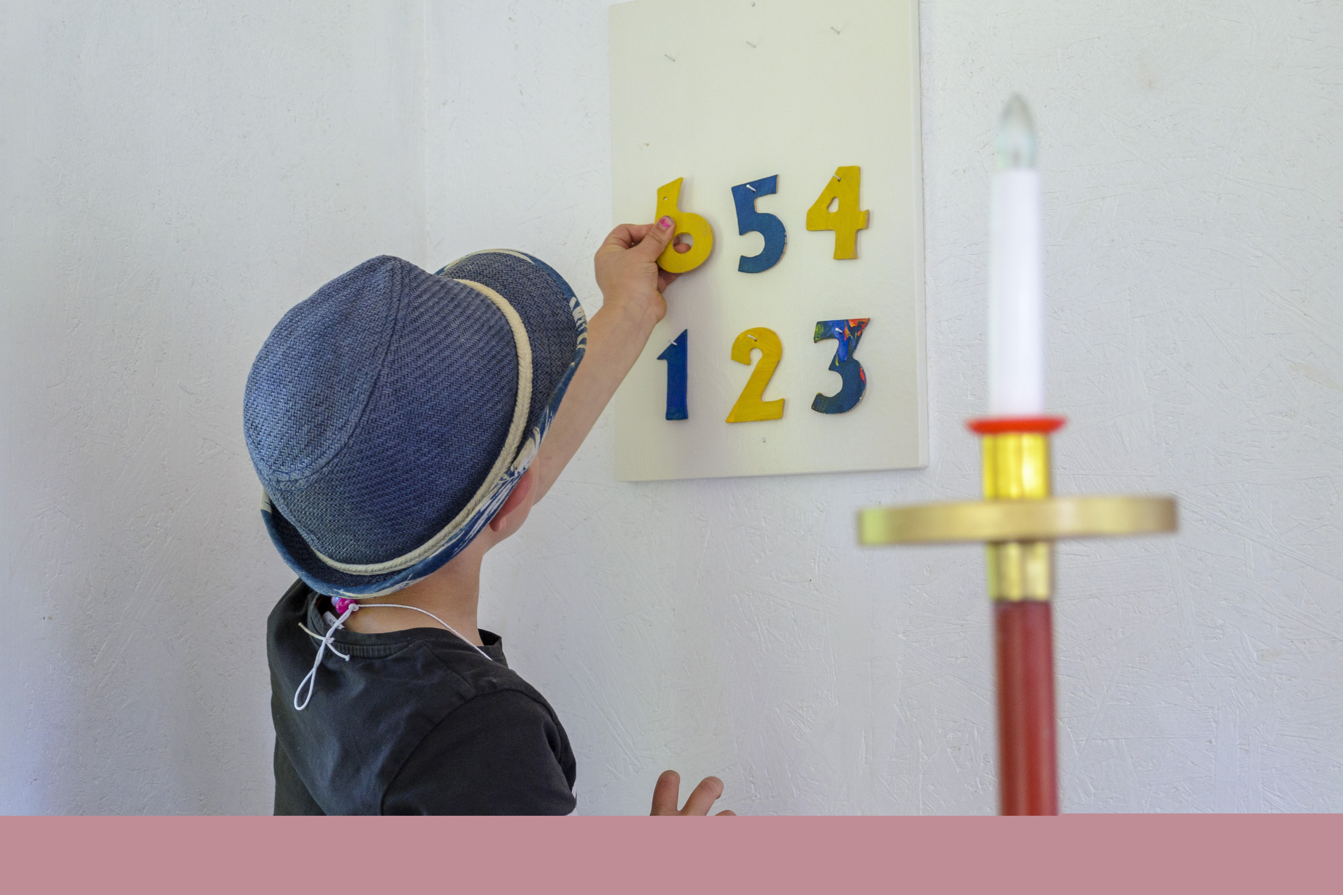 En pojke hänger upp färgglada siffror på en tavla på en psalmtavla. Ett släckt elektriskt ljus i förgrunden.