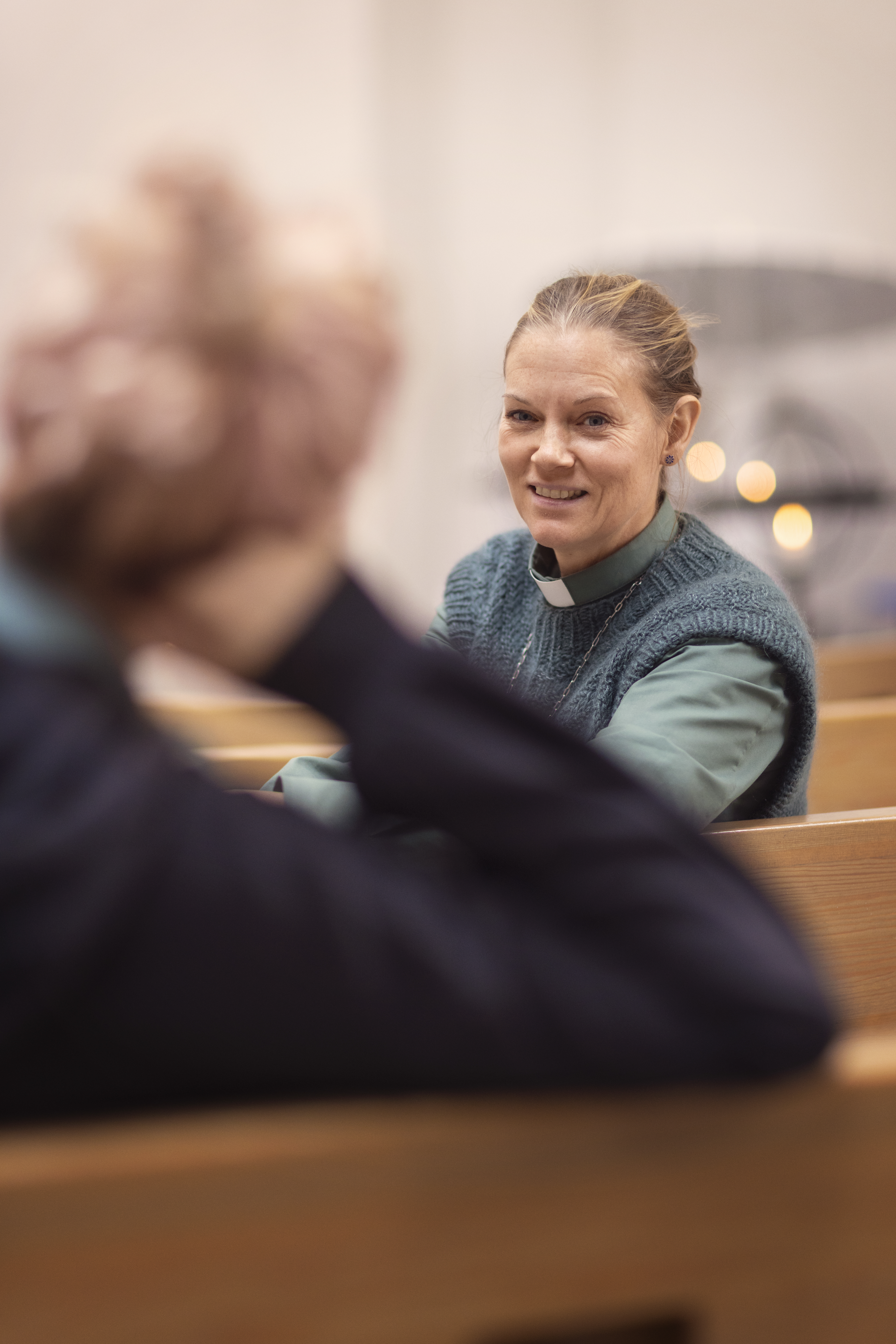 En kvinnlig diakon sitter med någon i kyrkbänken och samtalar.