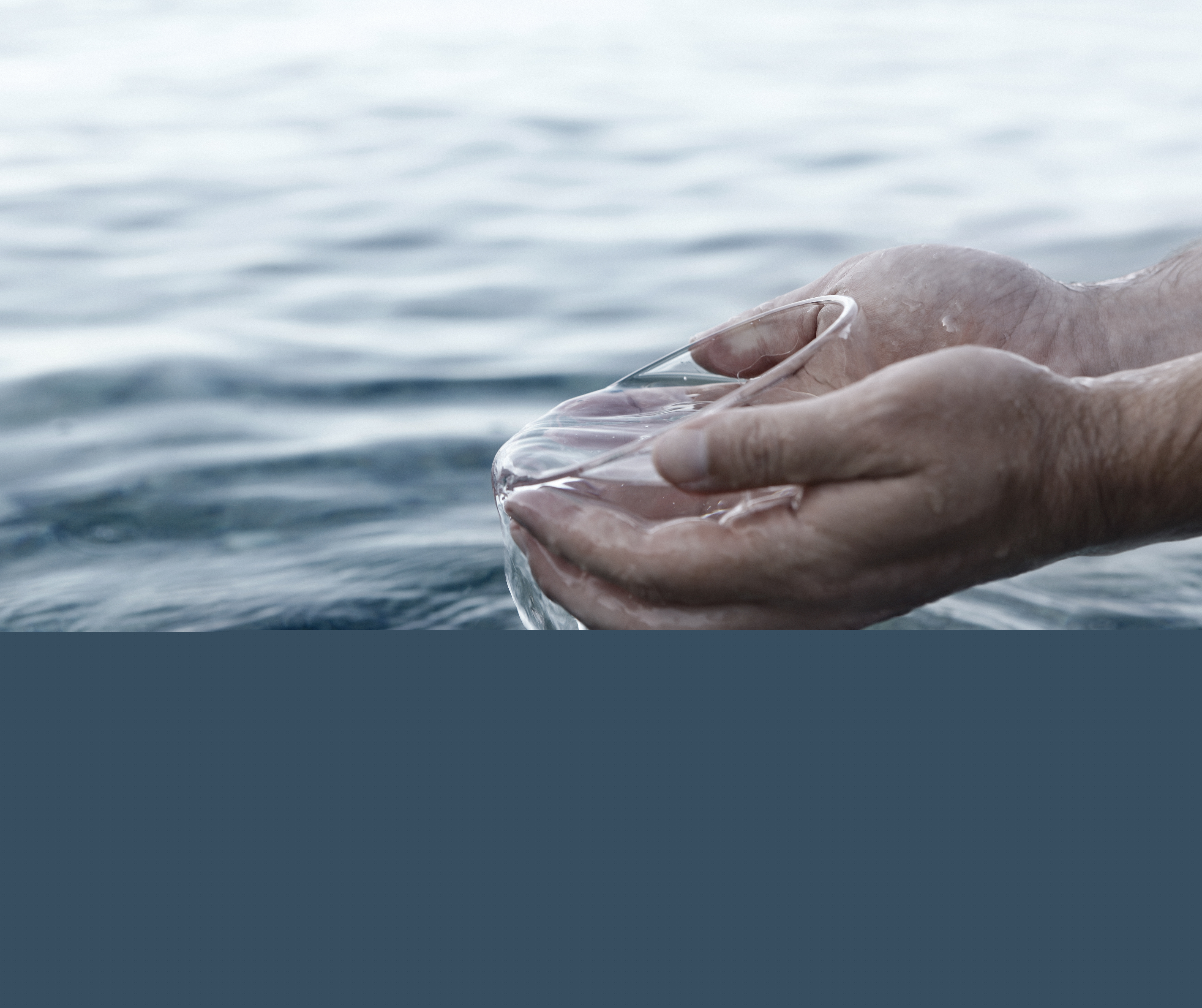 Händer håller i en glasskål med vatten som lyfts upp ur en sjö.