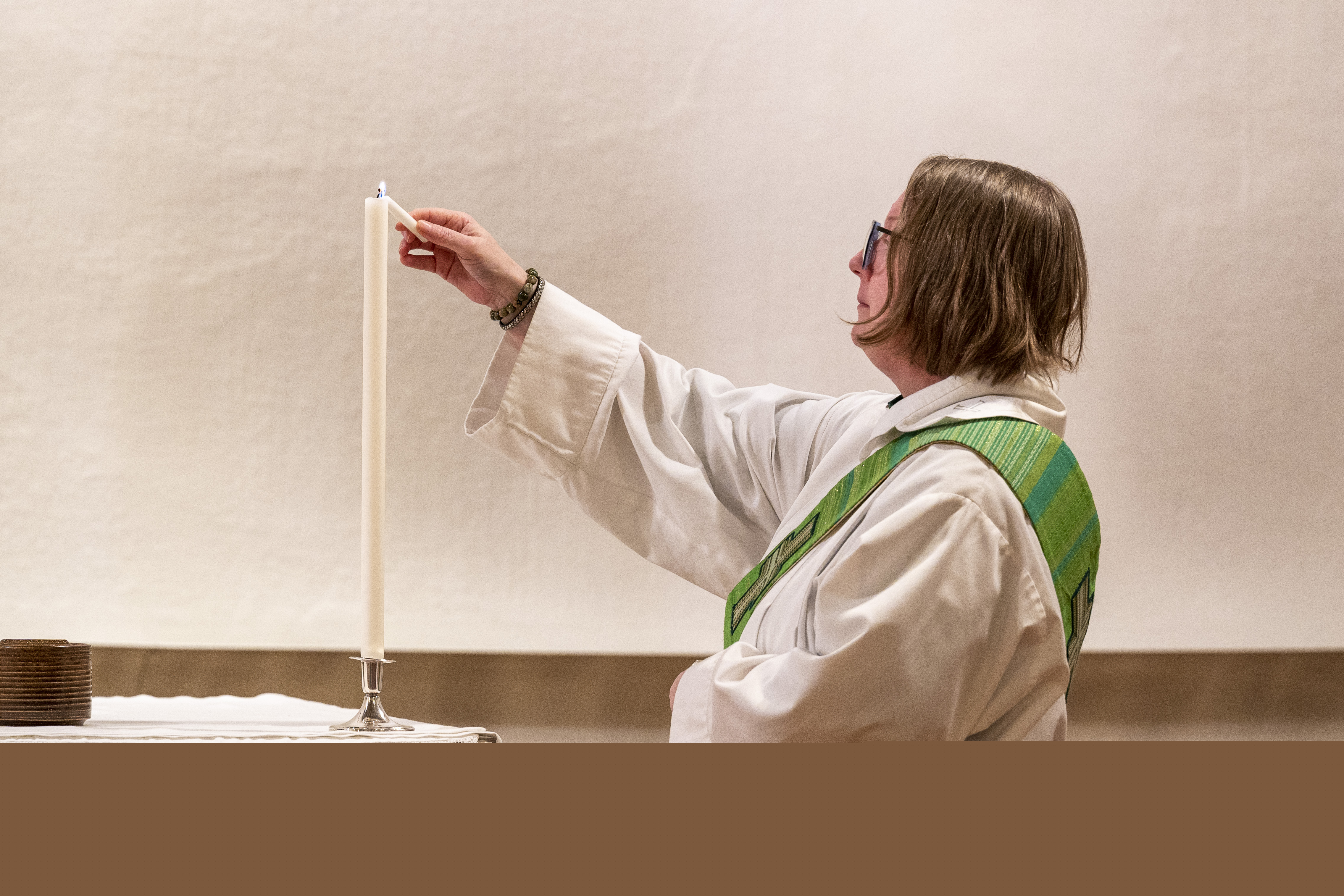 En kvinnlig diakon tänder ett ljus som står på altaret.
