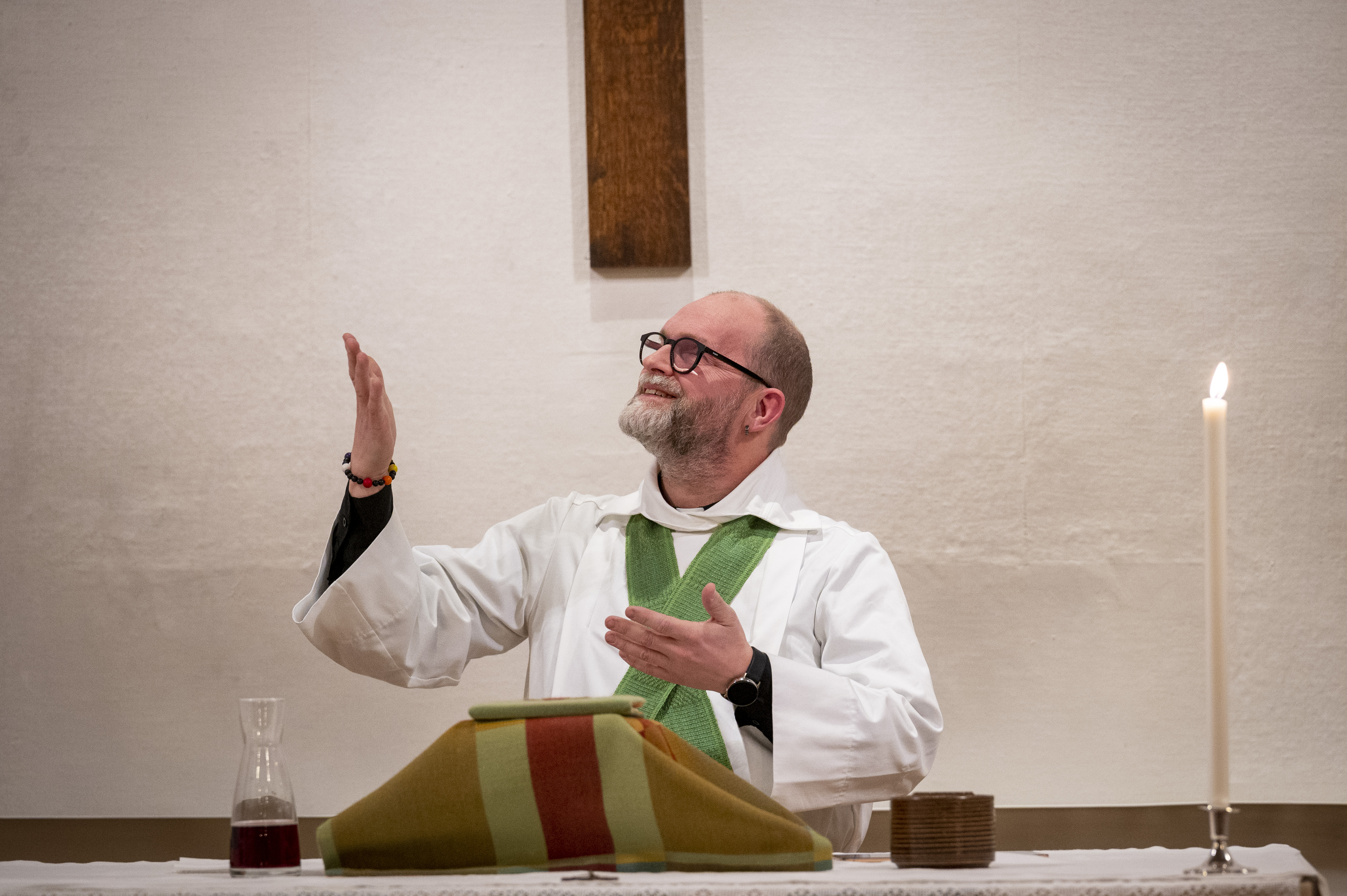 En manlig präst står vid altaret och gestikulerar med armarna.
