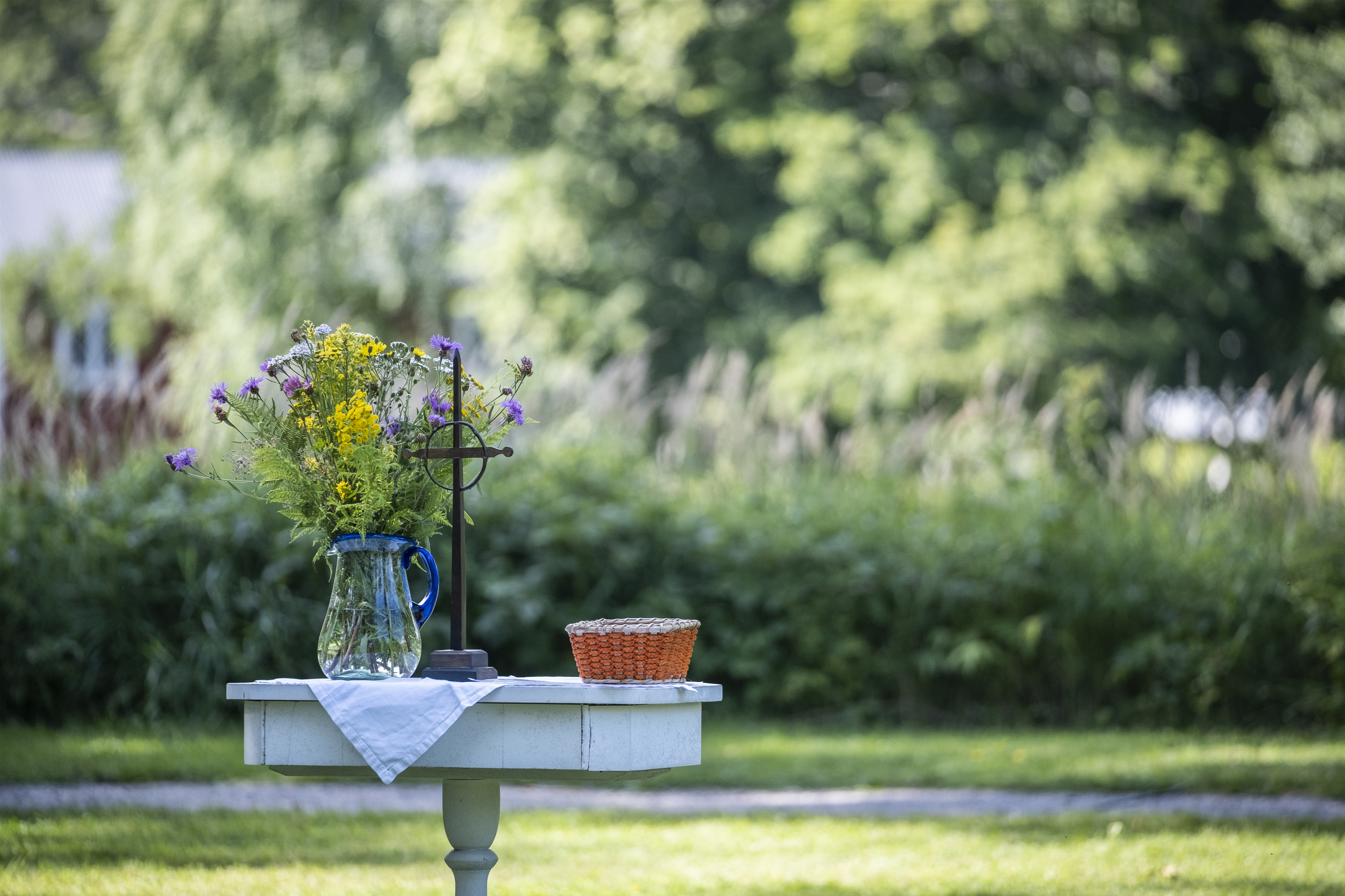Ett litet träbord har gjort till ett utomhusaltare utsmyckat med ett kors, en liten korg och en blombukett i en vas.