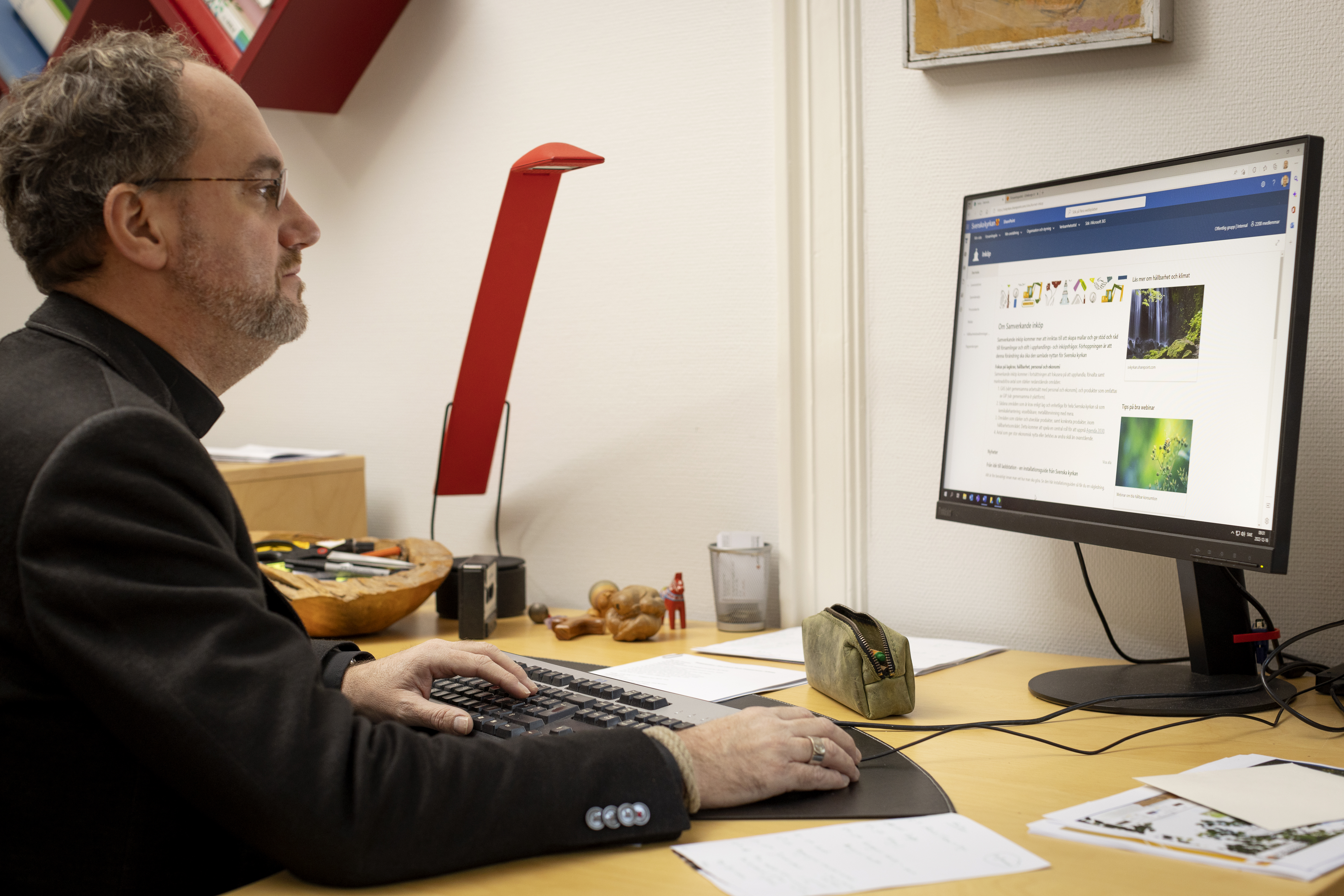 En man sitter vid ett skrivbord och arbetar i datorn.