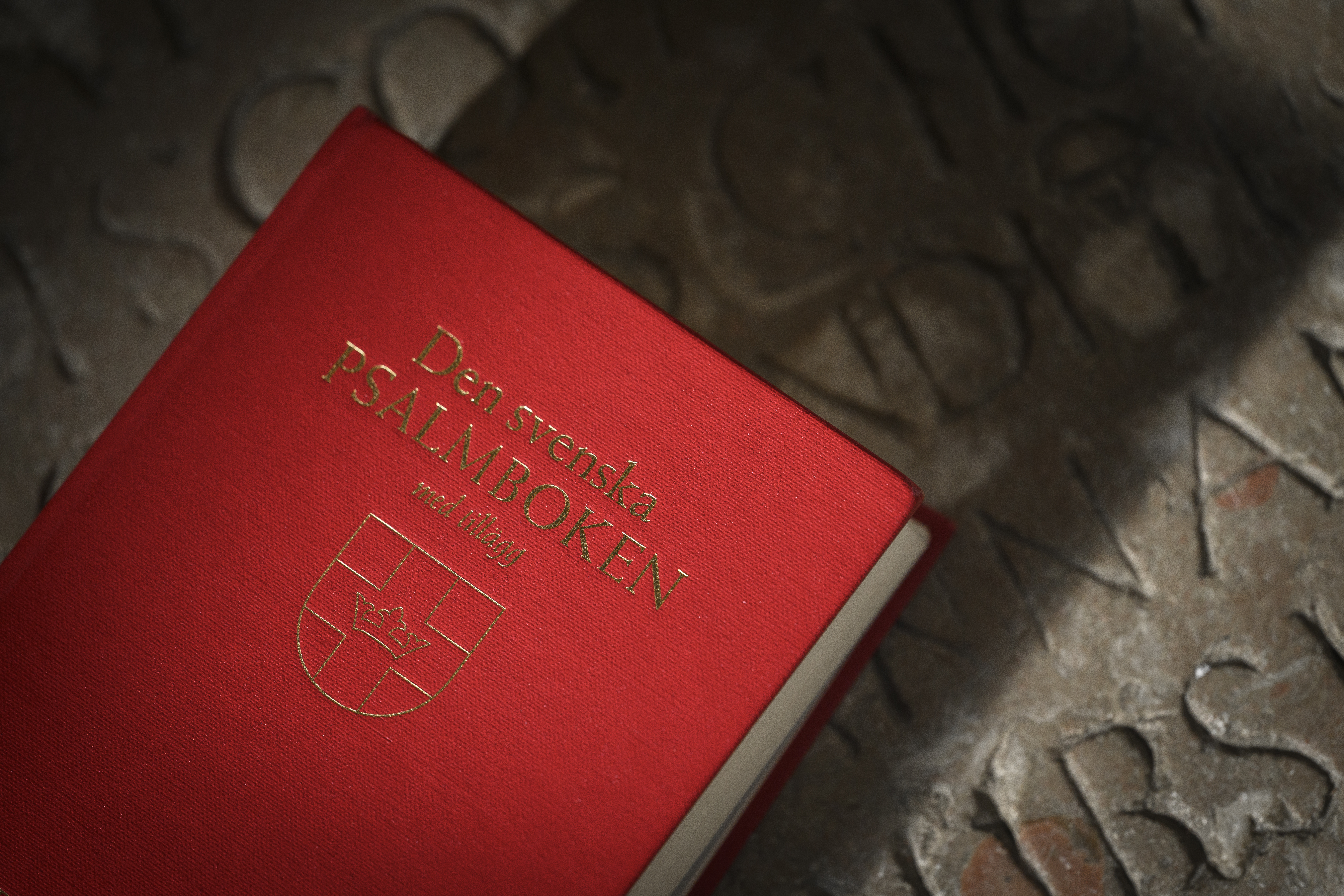 Närbild på en psalmbok som ligger på en golvsten med inristade bokstäver.