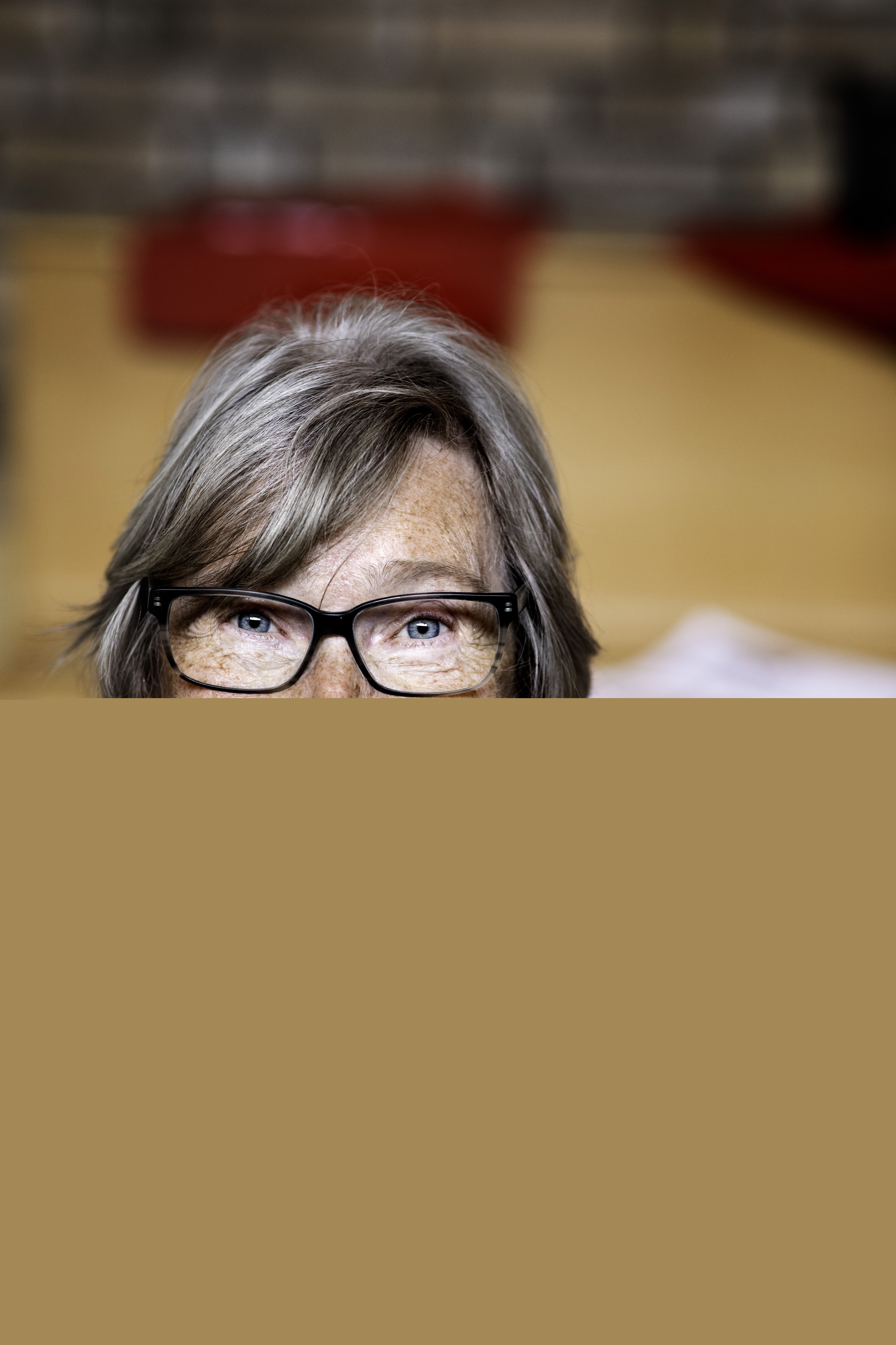 En kvinna med glasögon och färgglad blus håller upp en vit och blå stickning mot kameran.