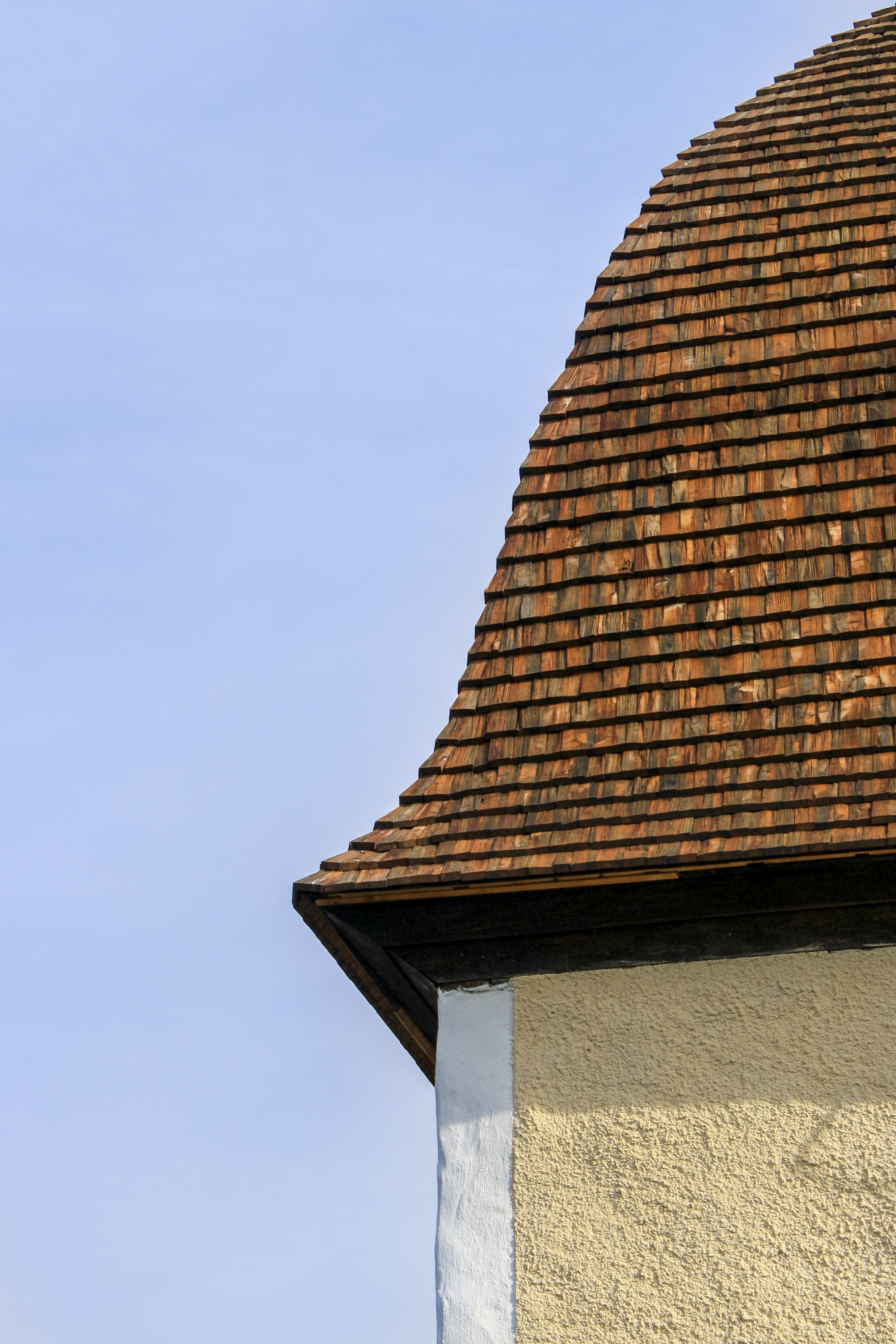 Ett kyrktorn med ett skiffertak mot blå himmel.