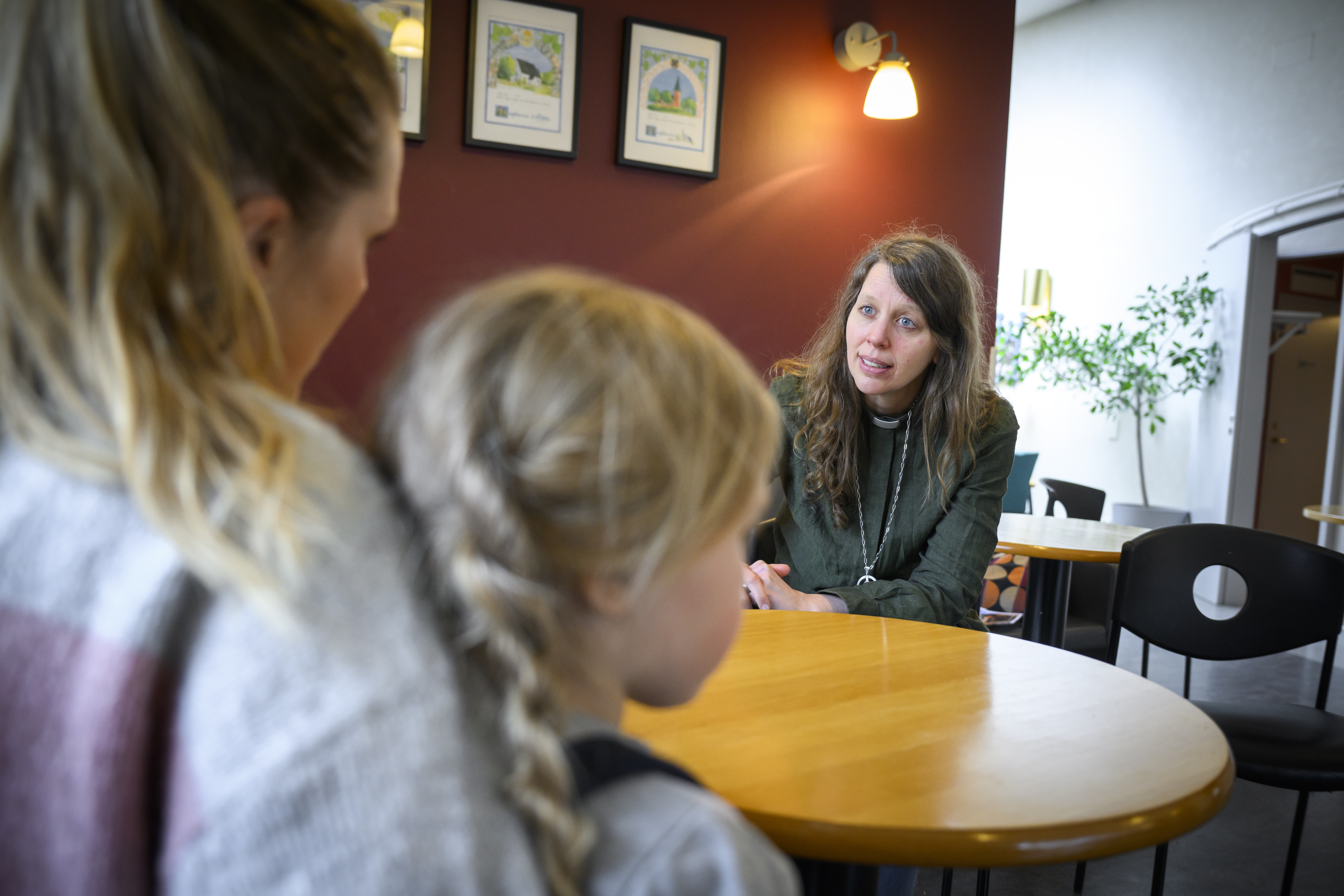 En diakon sitter och samtalar med en kvinna och en liten flicka.