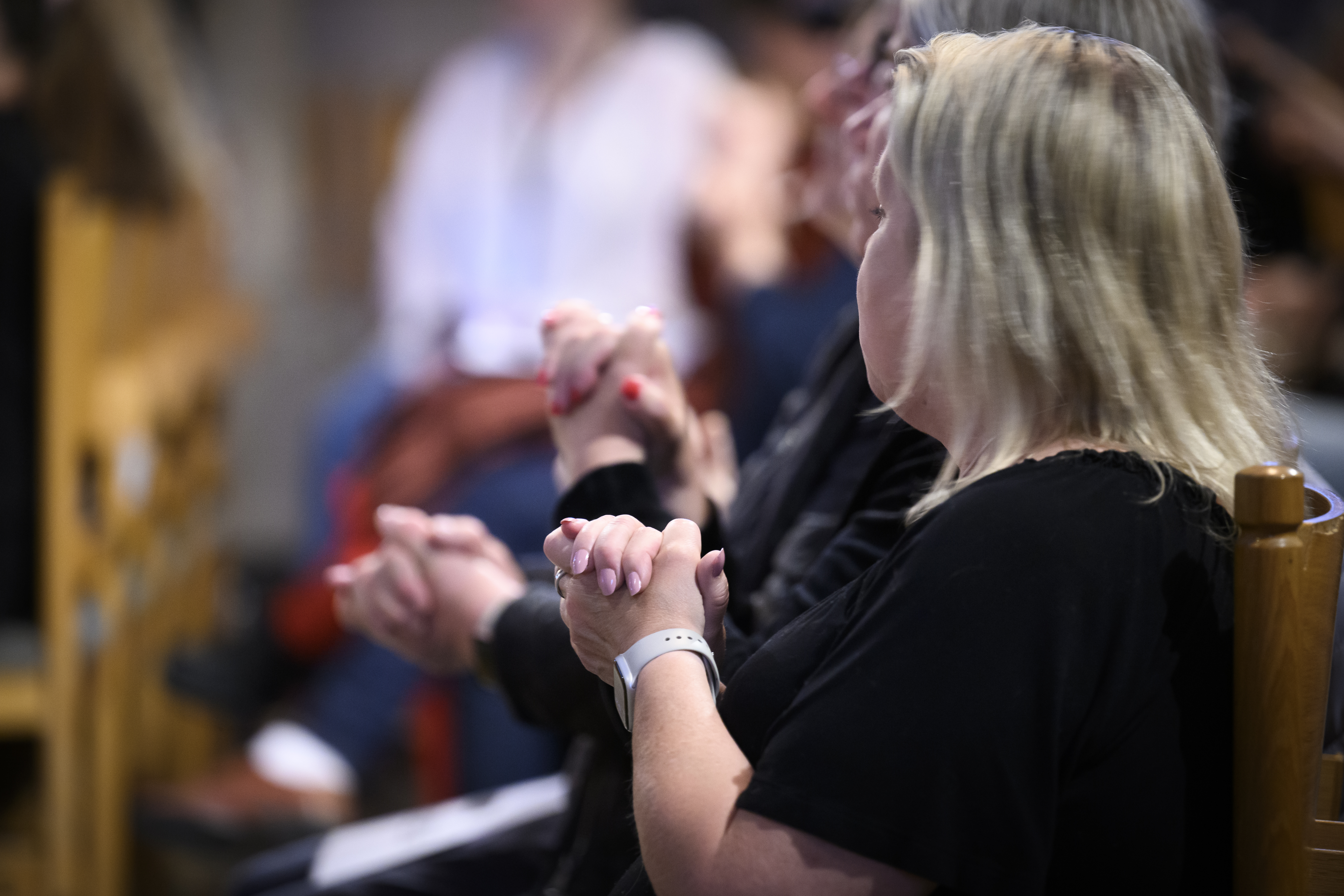 Människor i en bänkrad har lagt samman sina handflator och håller upp dem framför sig.