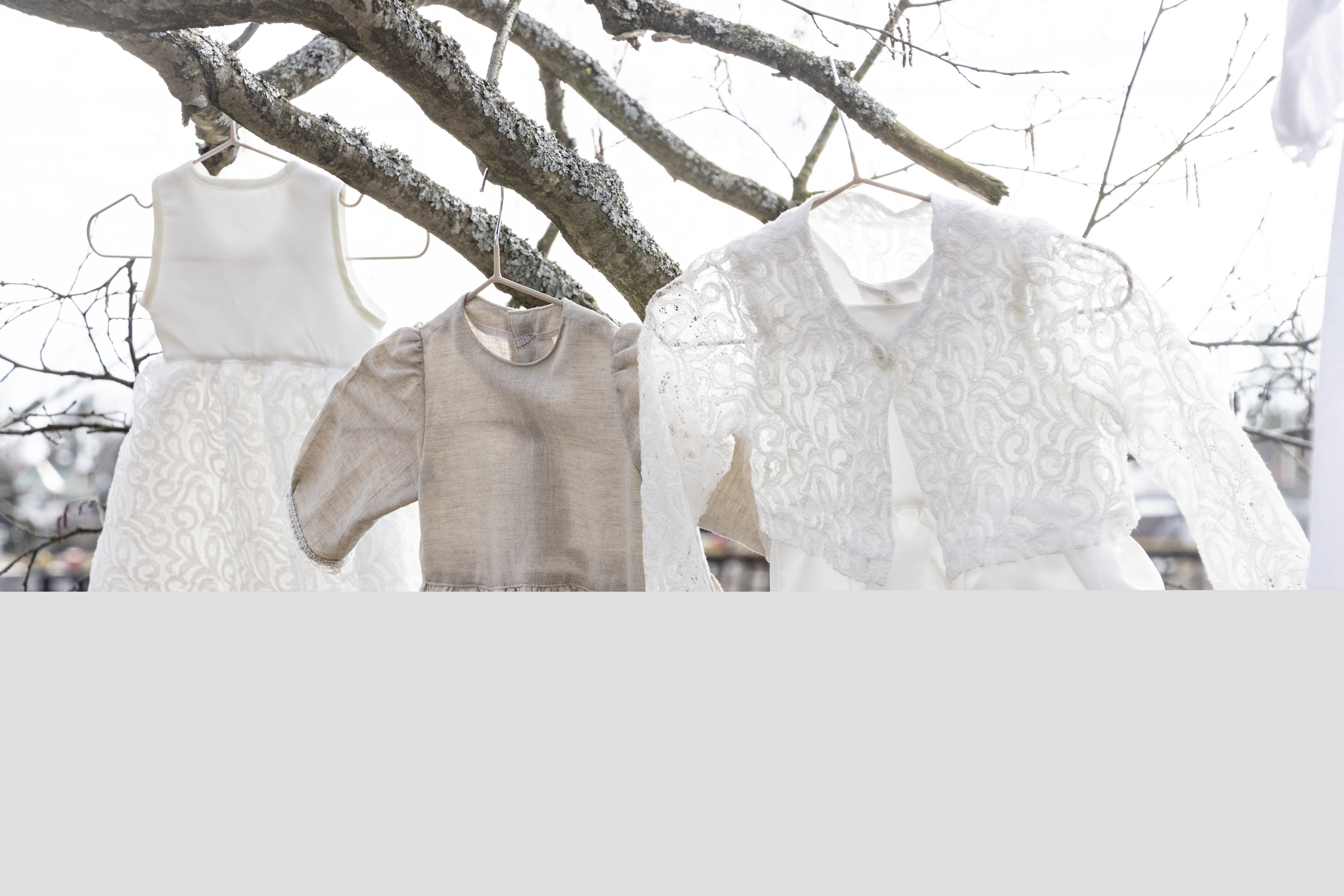 Tre olika dopklänningar hänger i ett träds grenar.