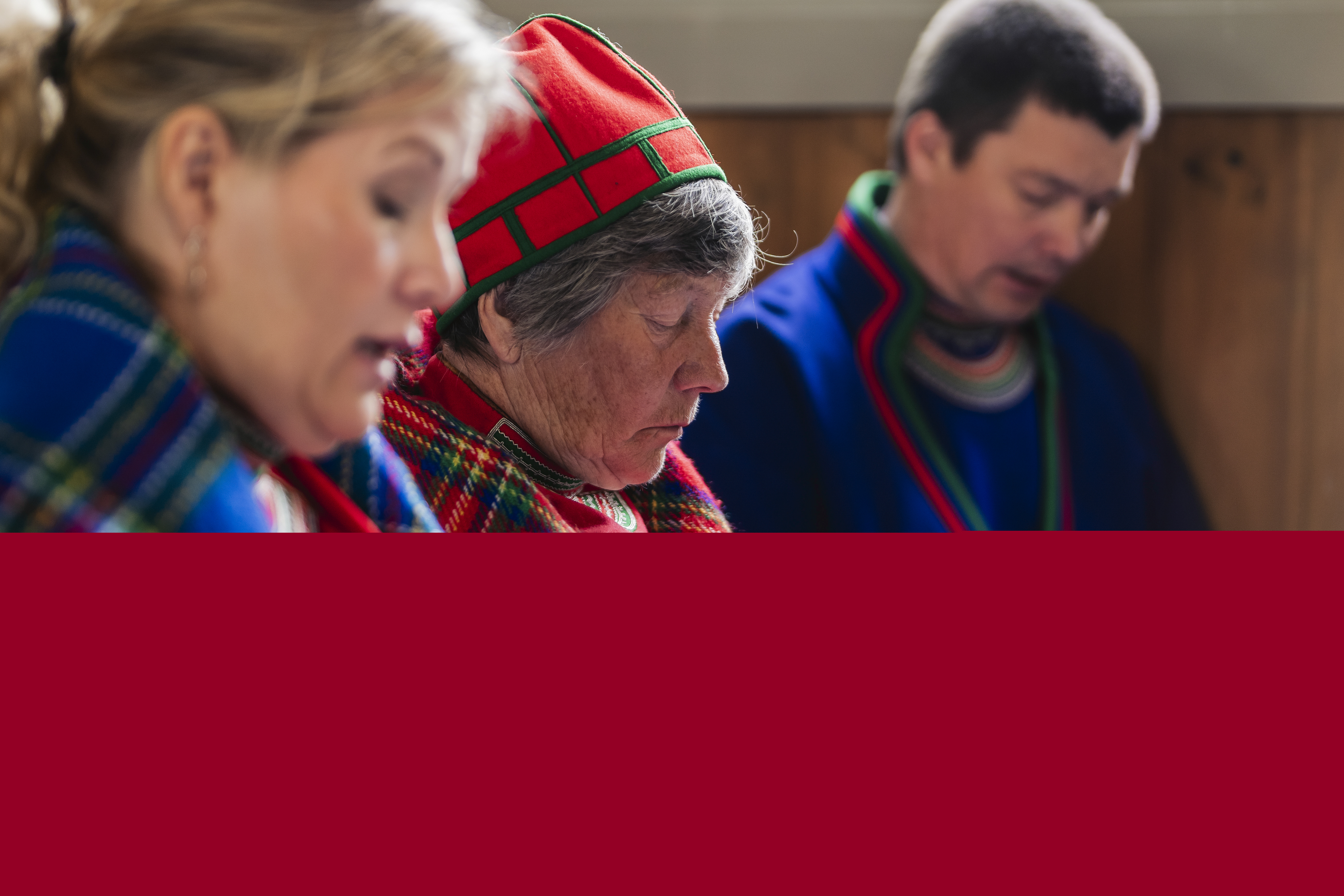 Tre personer i samiska kläder sjunger i kyrkbänken.