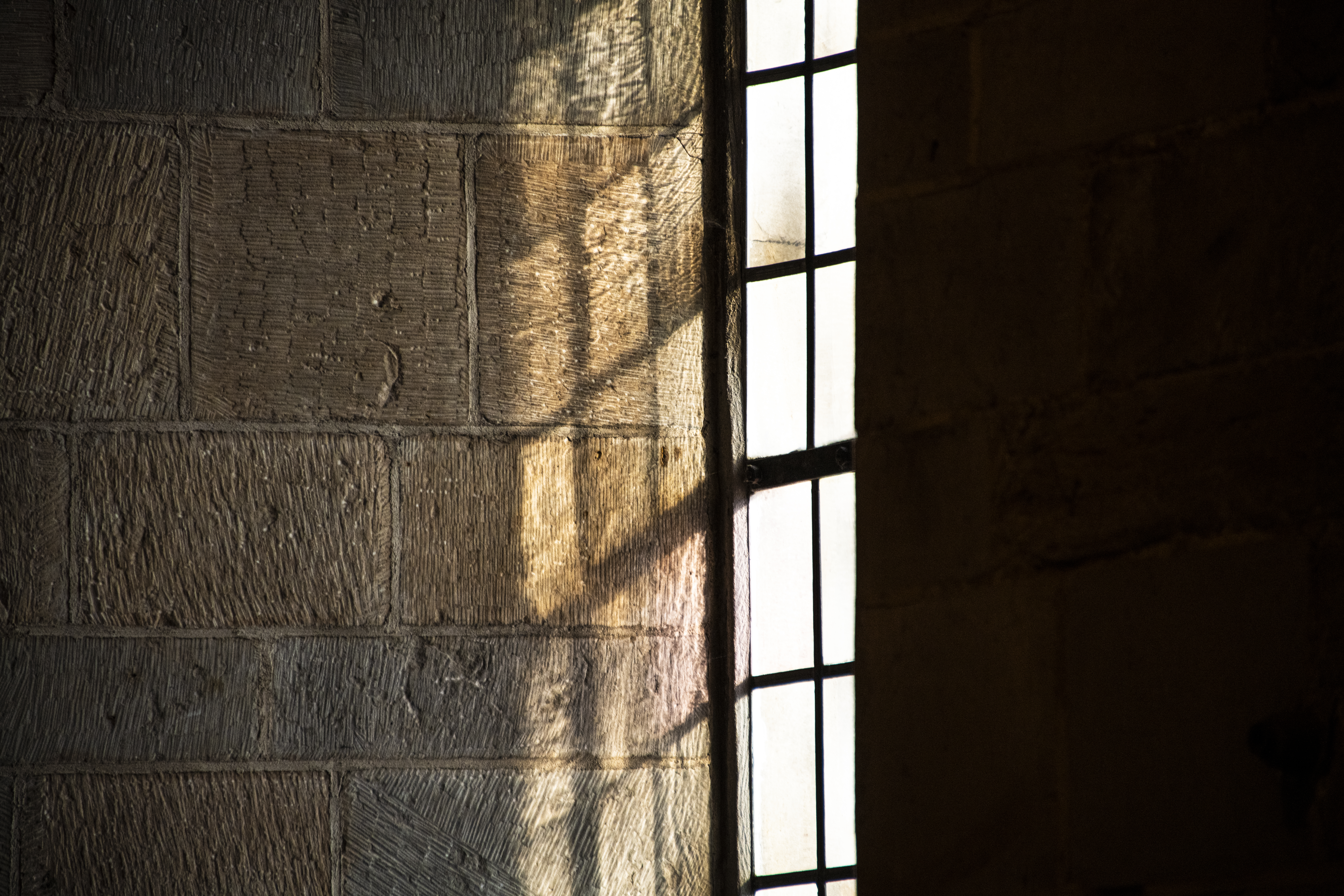 Solen lyser på en stenvägg genom ett kyrkfönster.