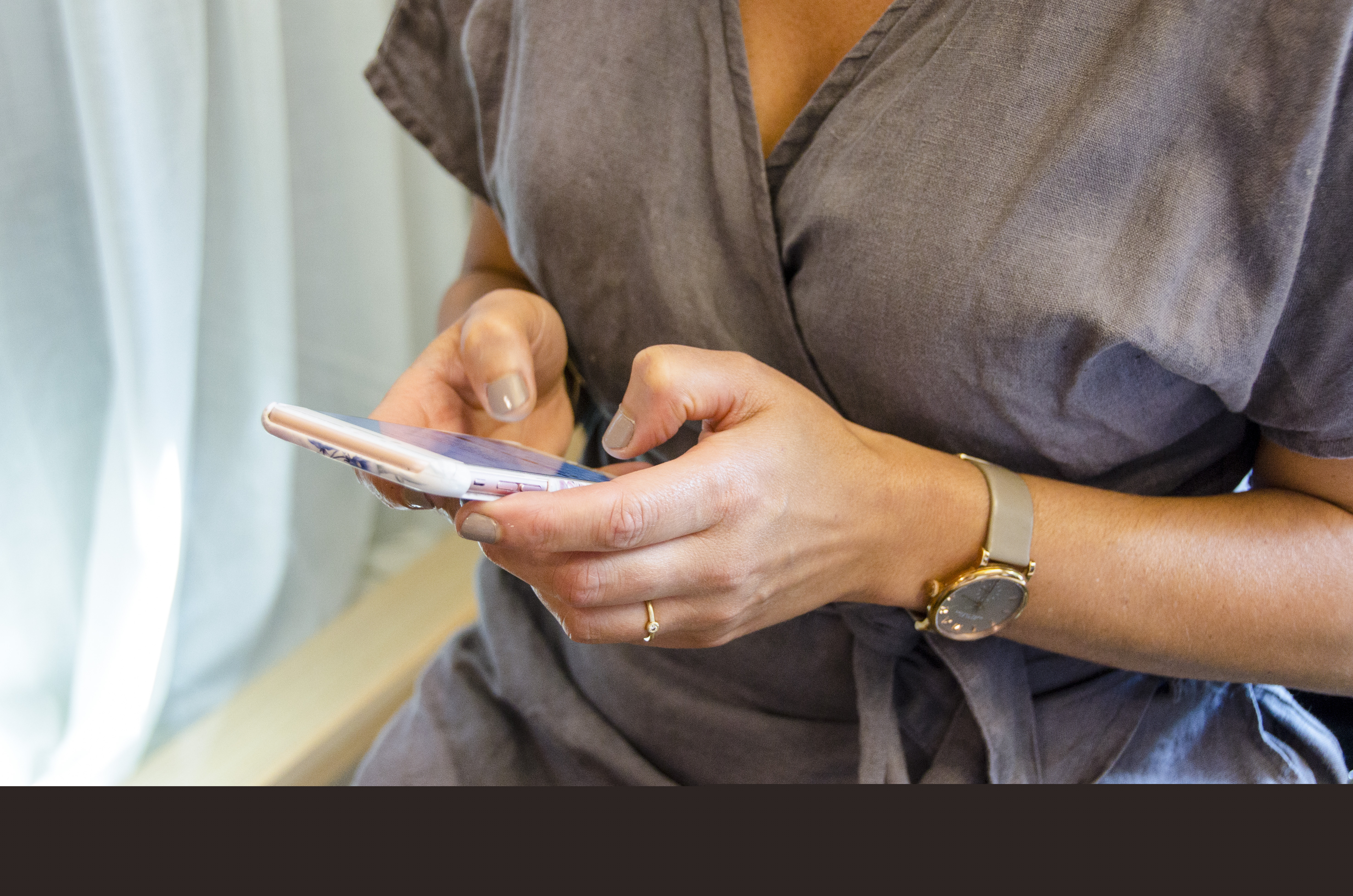 En kvinna med grå blus knappar på en smartphone.