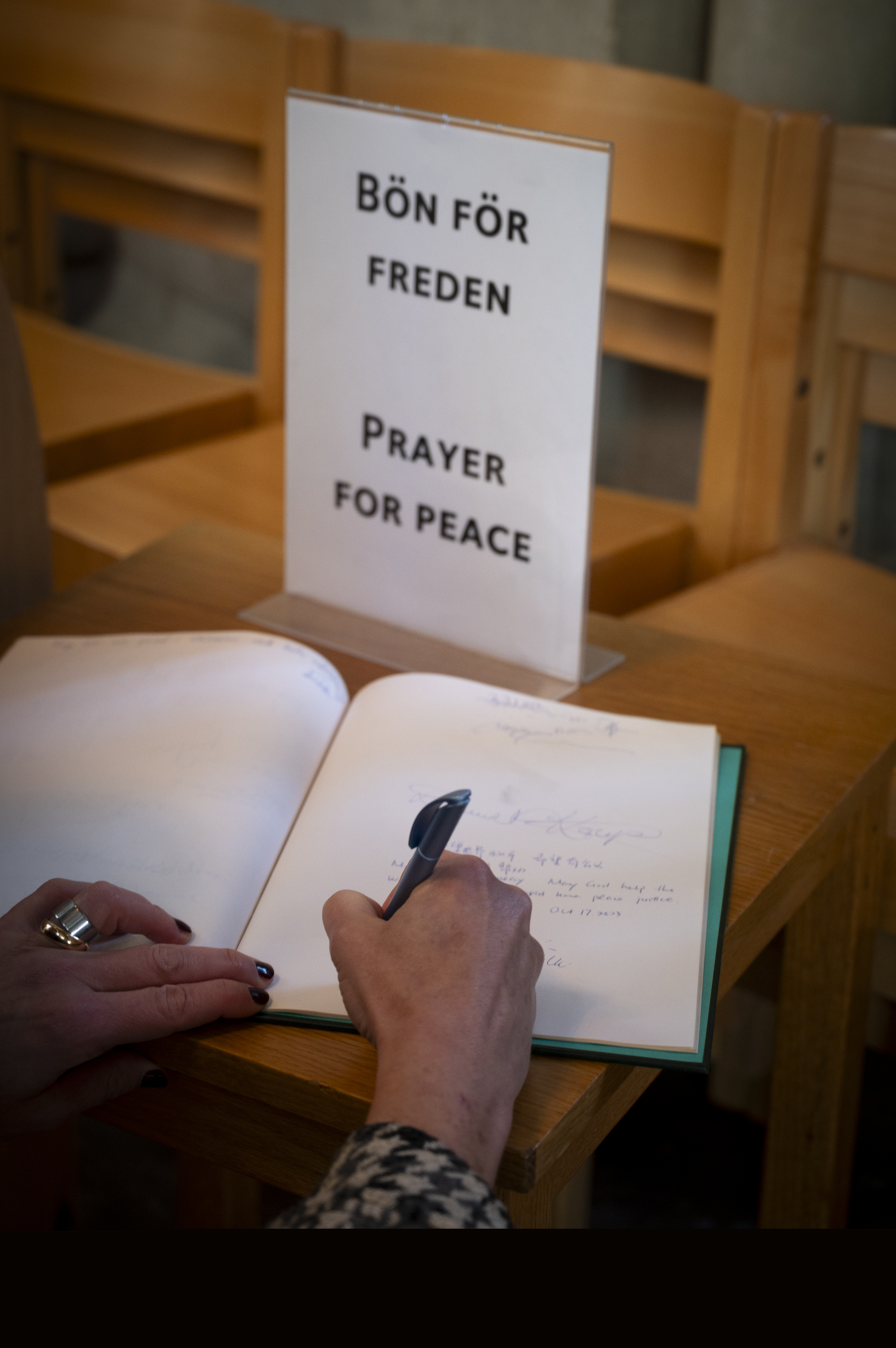 Någon skriver i en bok med blanka blad. En skylt med texten Bön för freden står bredvid.