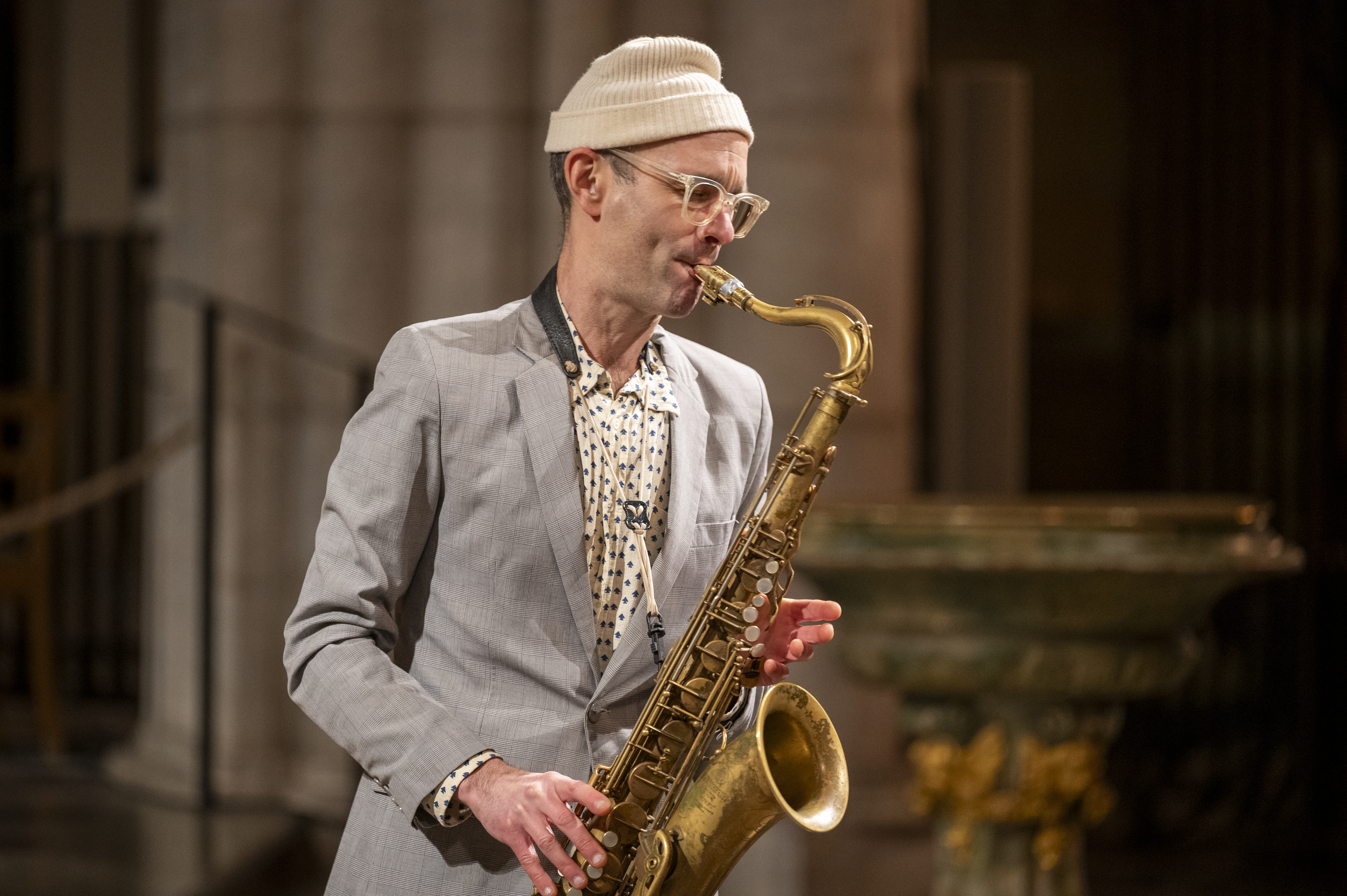 En man i ljusgrå kostym och vit mössa spelar saxofon i Uppsala domkyrka.