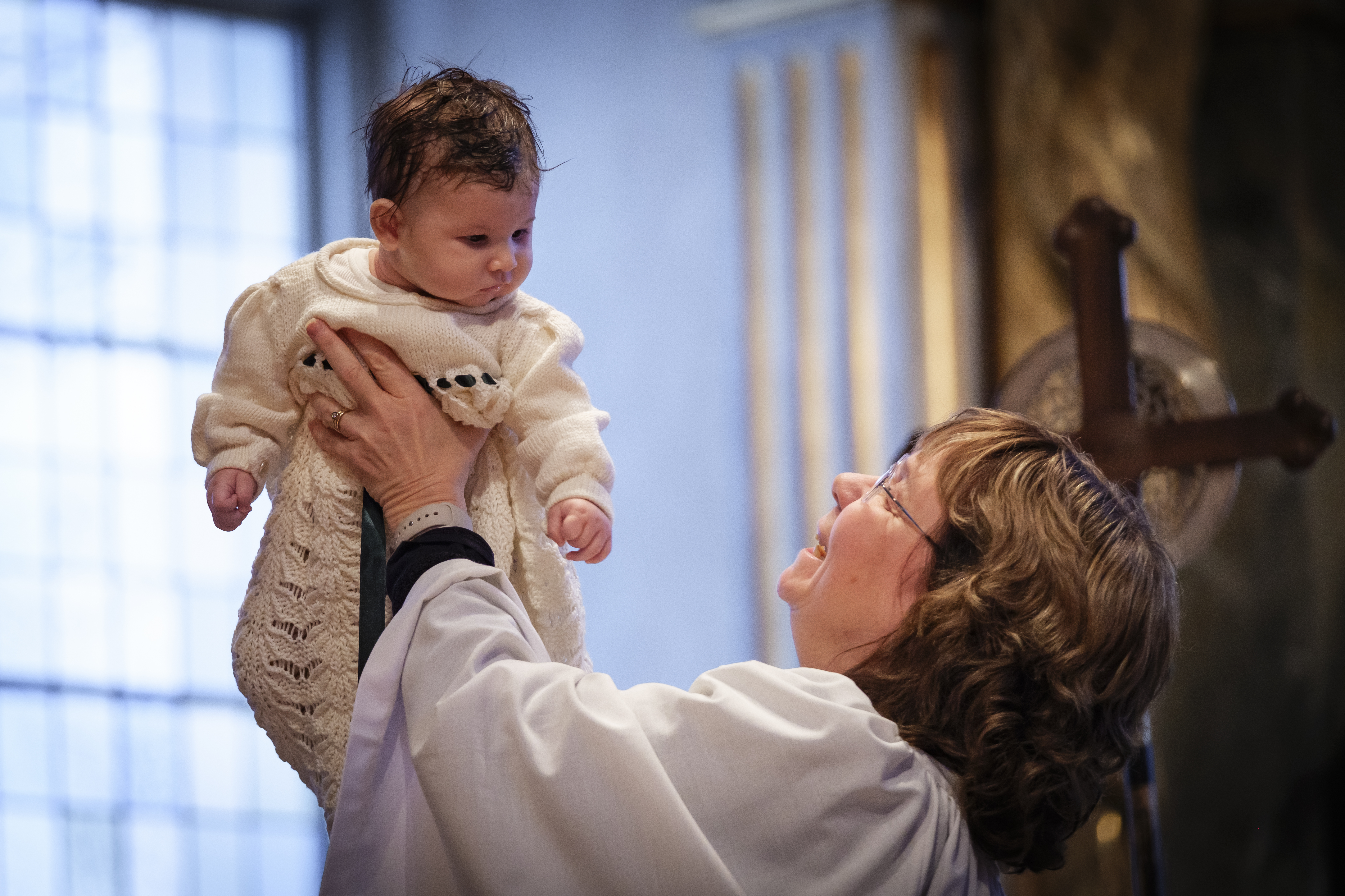 En kvinnlig präst håller upp en bebis som precis har döpts.