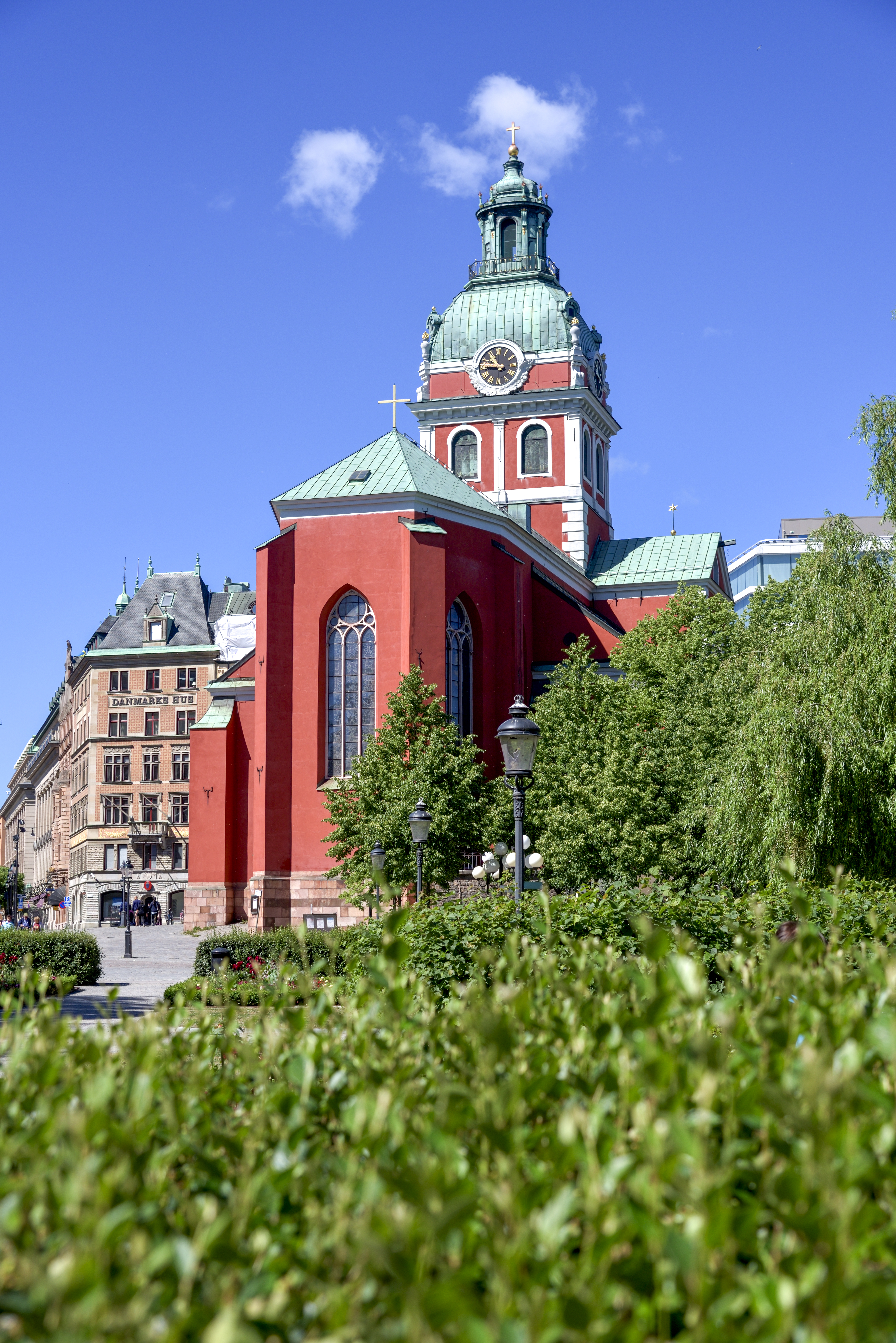 En röd stenkyrka med grönt koppartak i stadsmiljö.