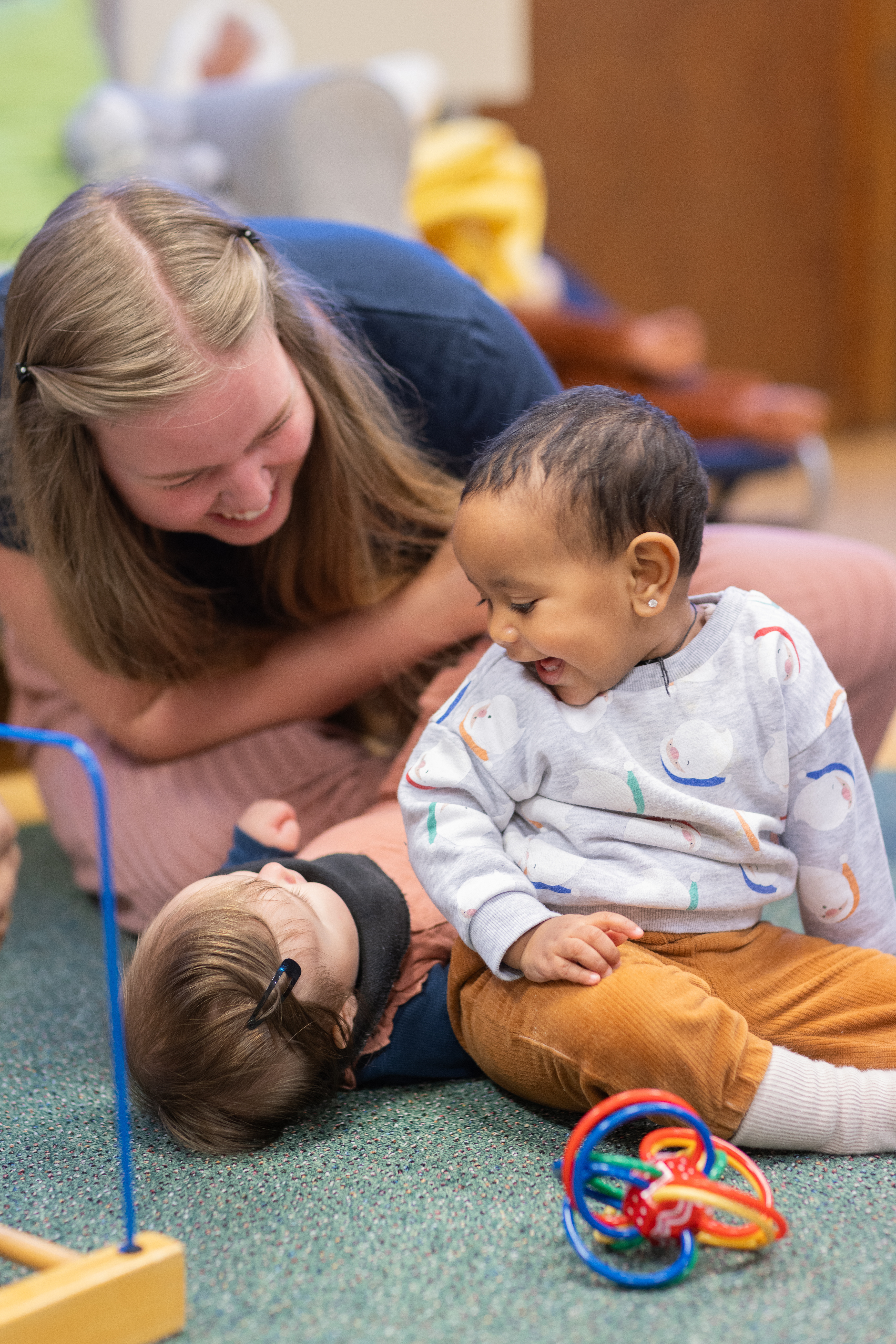 Två bebisar och en mamma skrattar på golvet.
