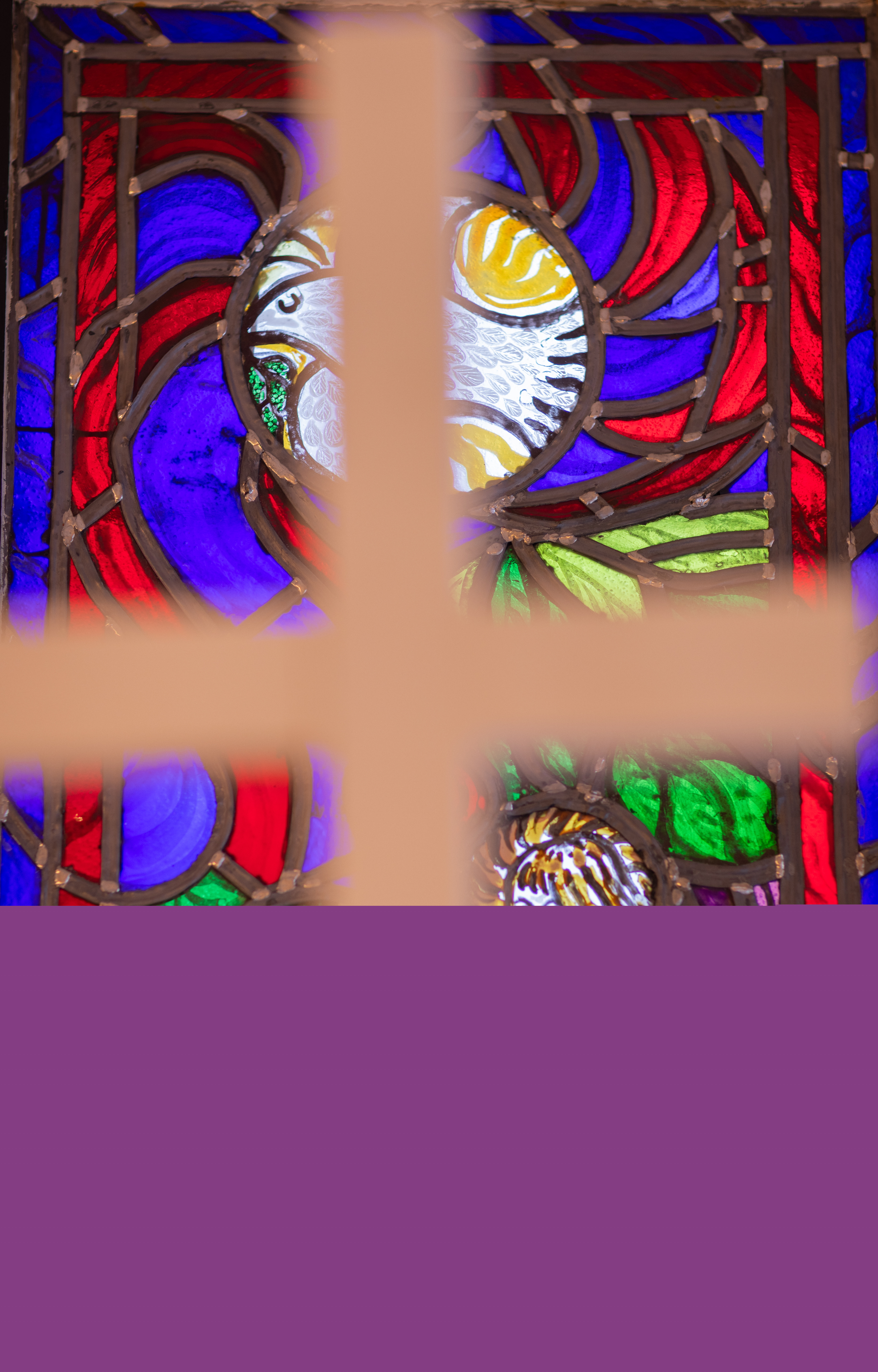 Ett oskarpt kors i förgrund av ett kyrkfönster, vi ser en fredsduva i glaset.