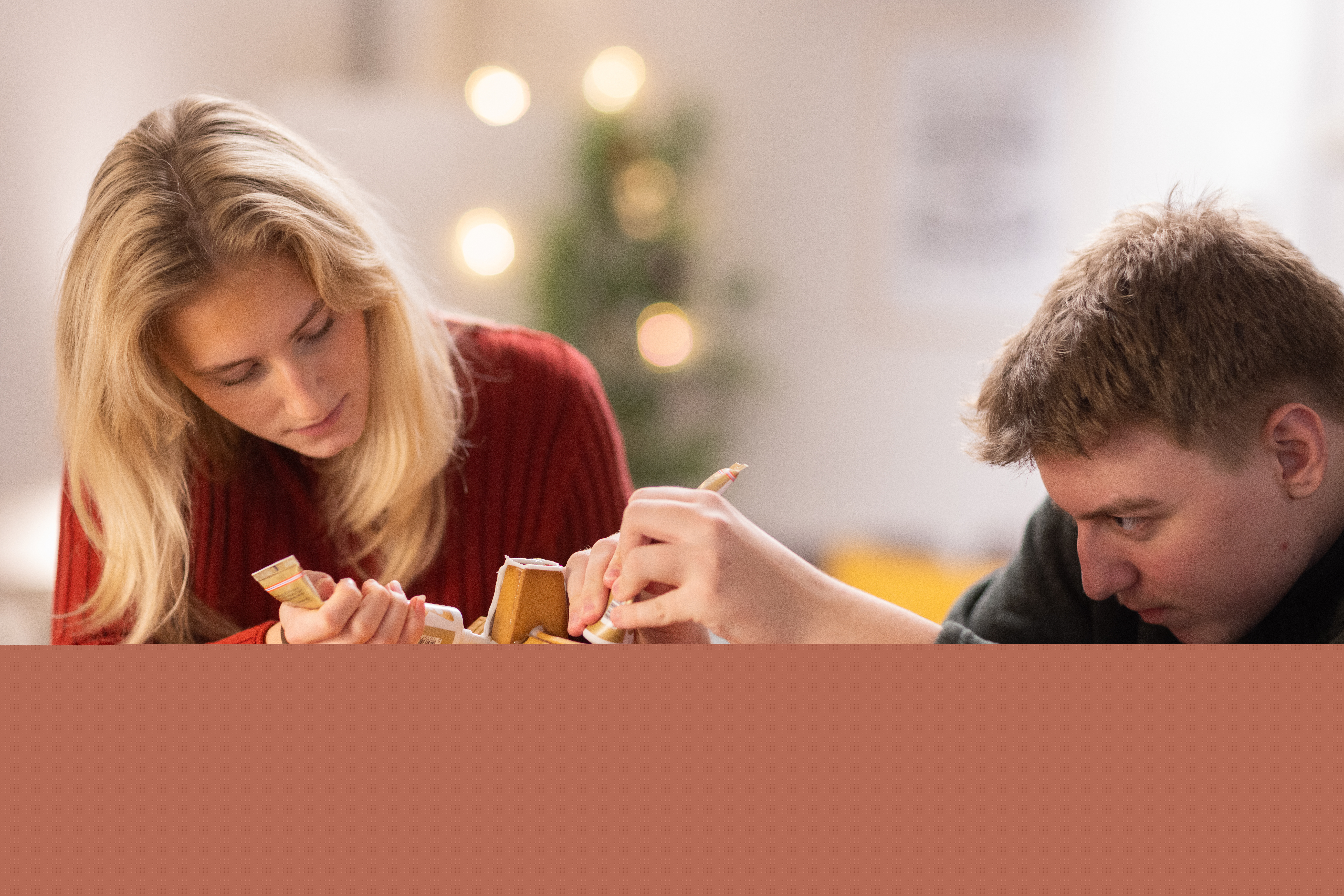 En tjej och en kille i tonåren spritsar ett pepparkakshus.