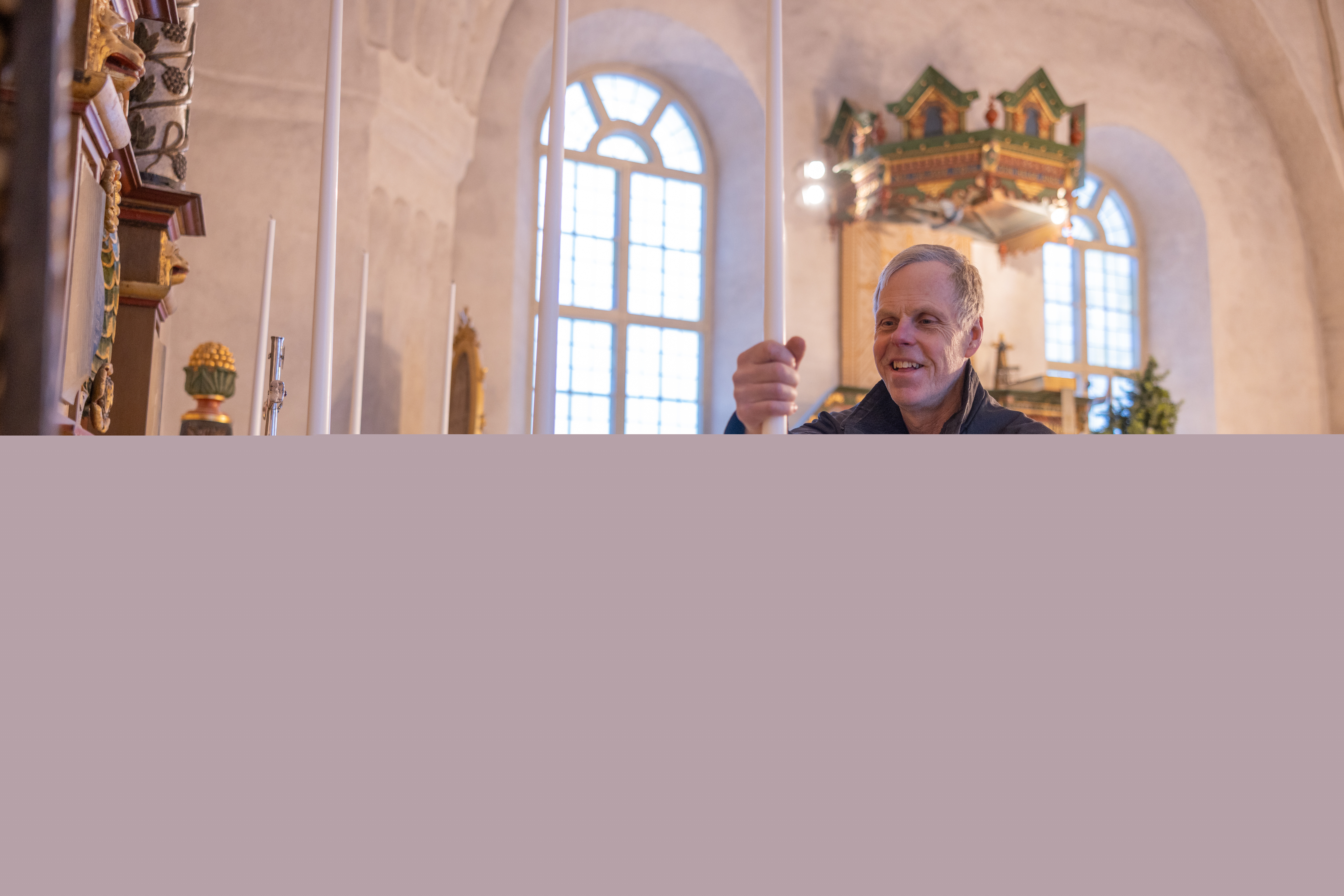 En kyrkvaktmästare sätter långa stearin ljus i de gyllene ljusstakarna på kyrkans altare.