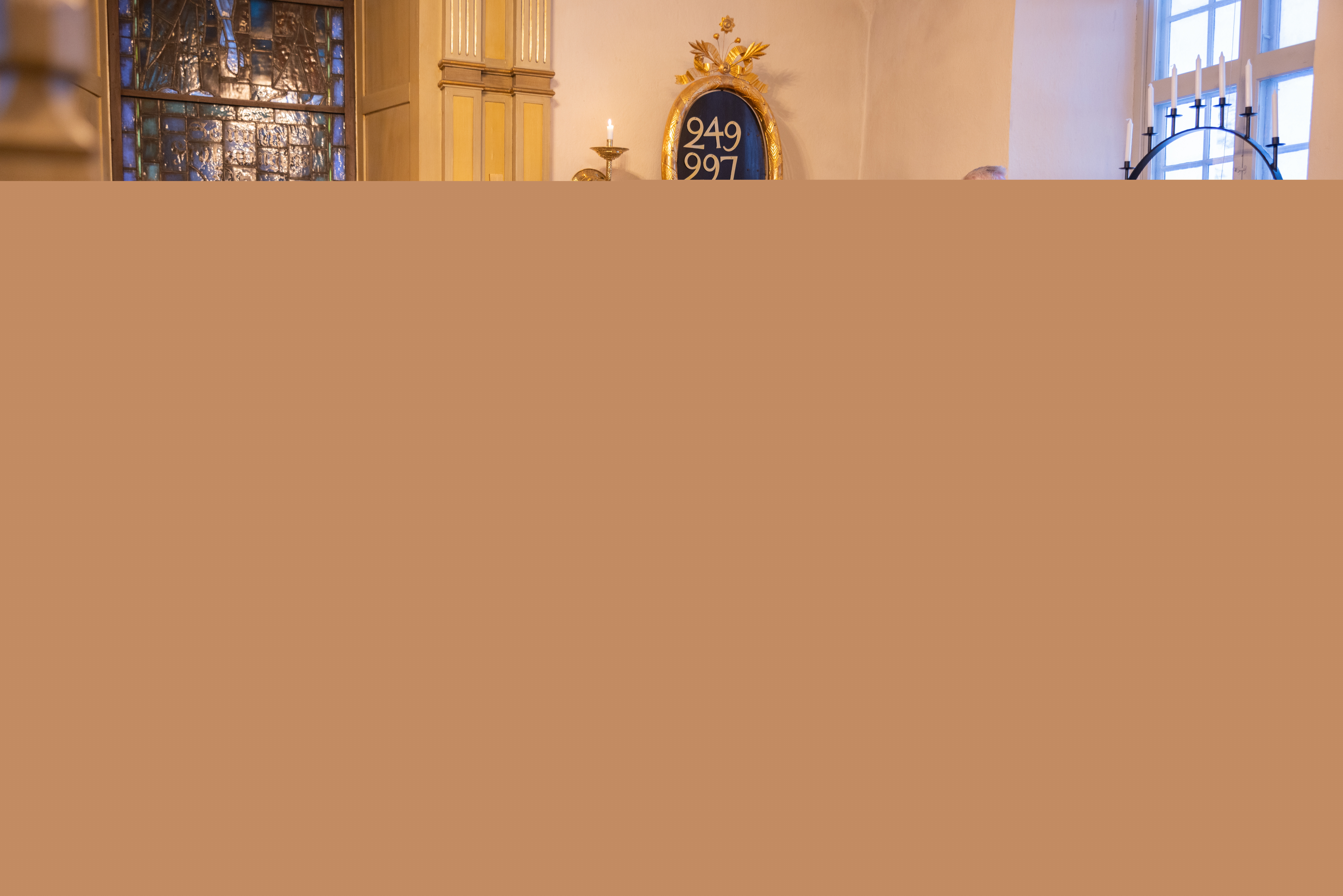 En kyrkvaktmästare tänder ljus i ett fönster. I koret står en vit kista med röda och vita blommor på.