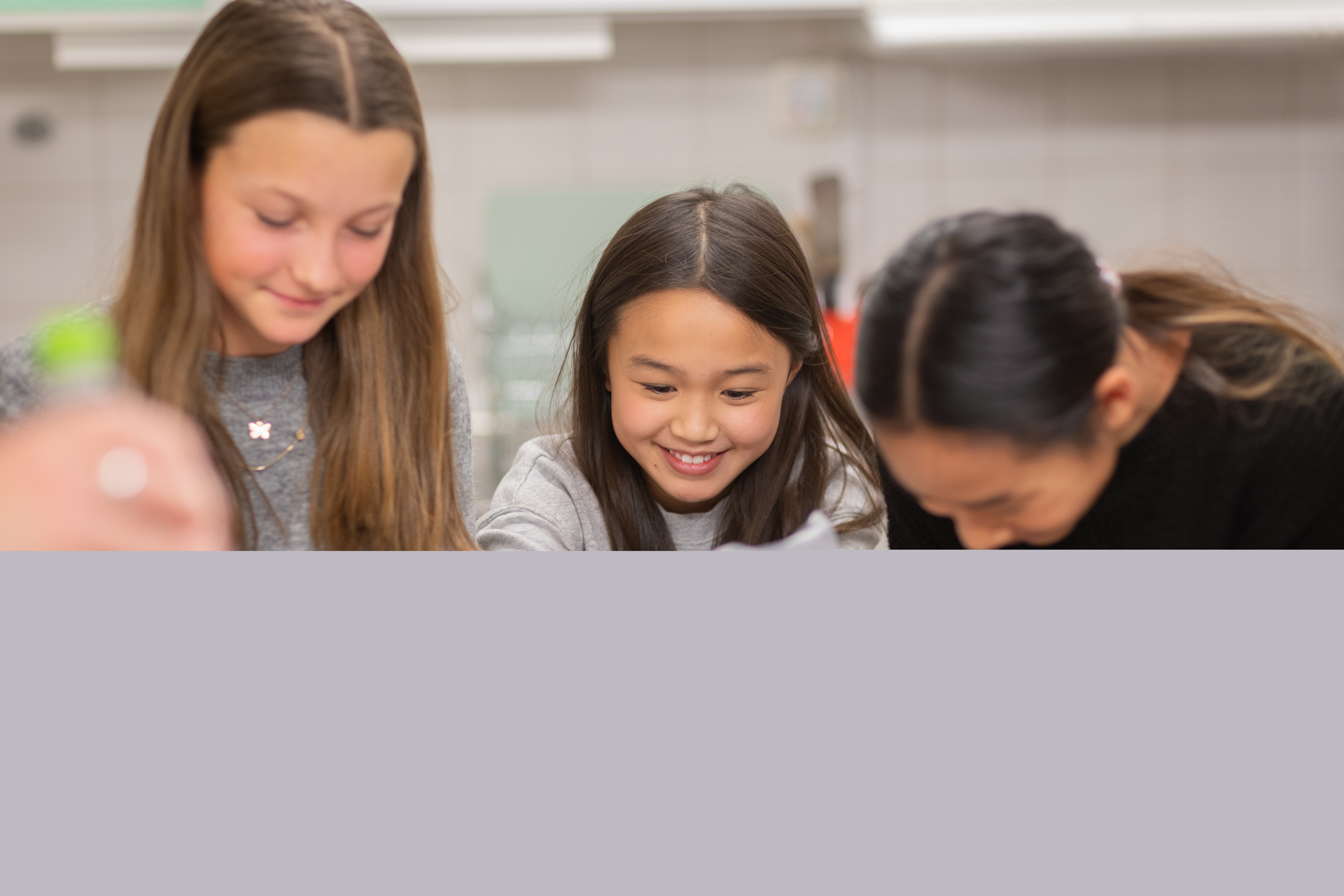 Tre skrattande flickor spritsar i ett kök.