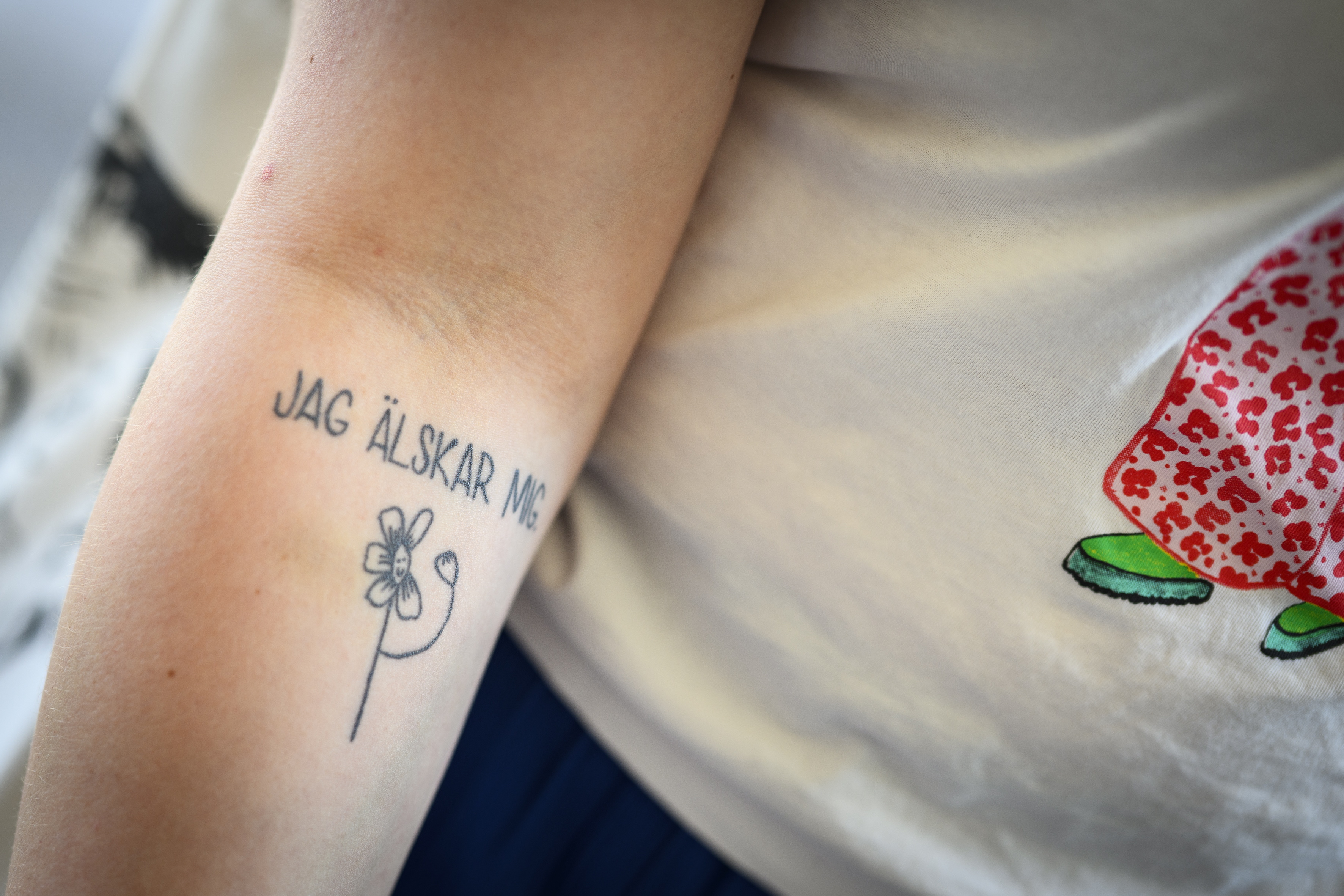 Närbild på en tatuerad arm med texten jag älskar mig och en blomma under.