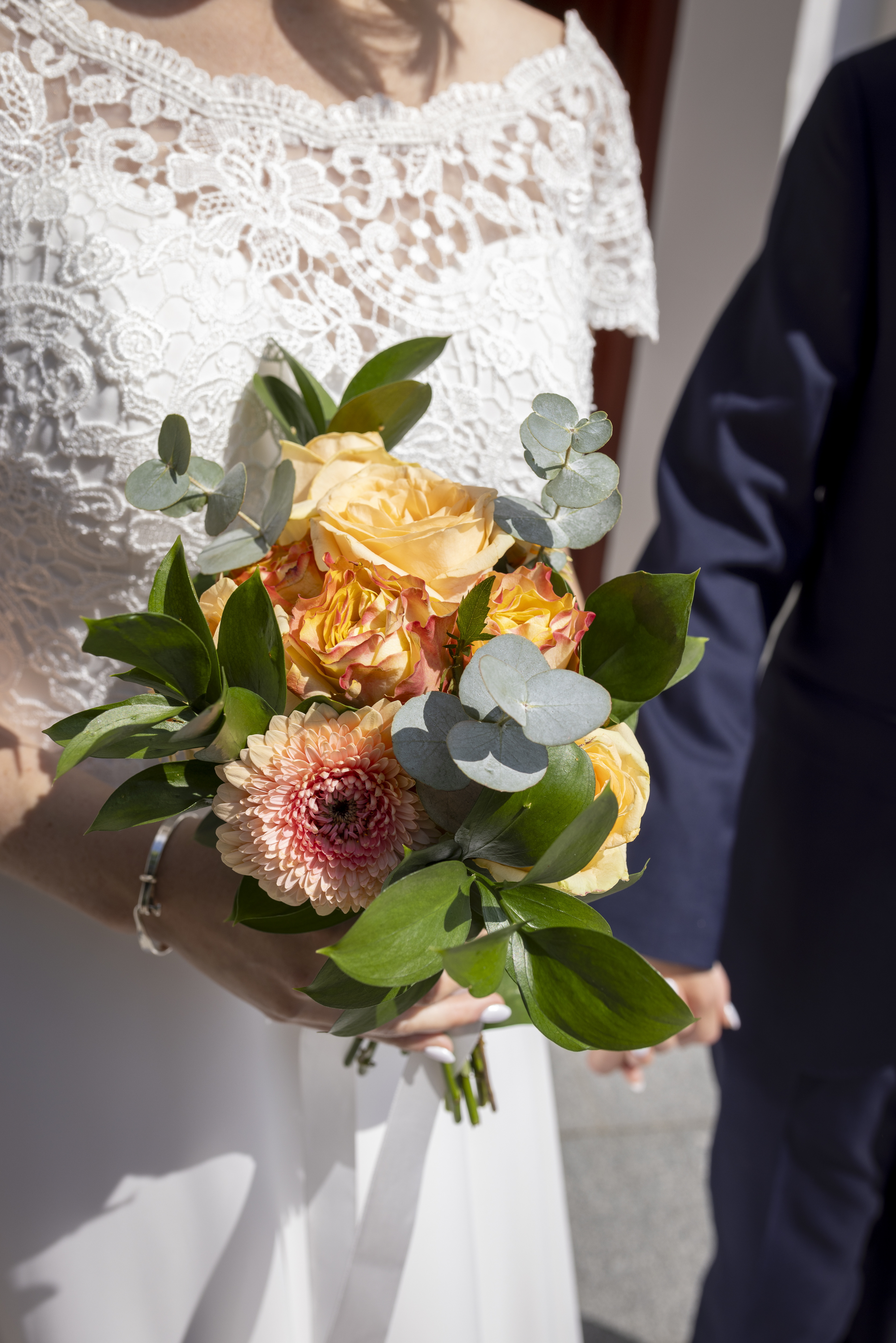 Närbild på en kvinna, i vit brudklänning med spets, som håller i en brudbukett.