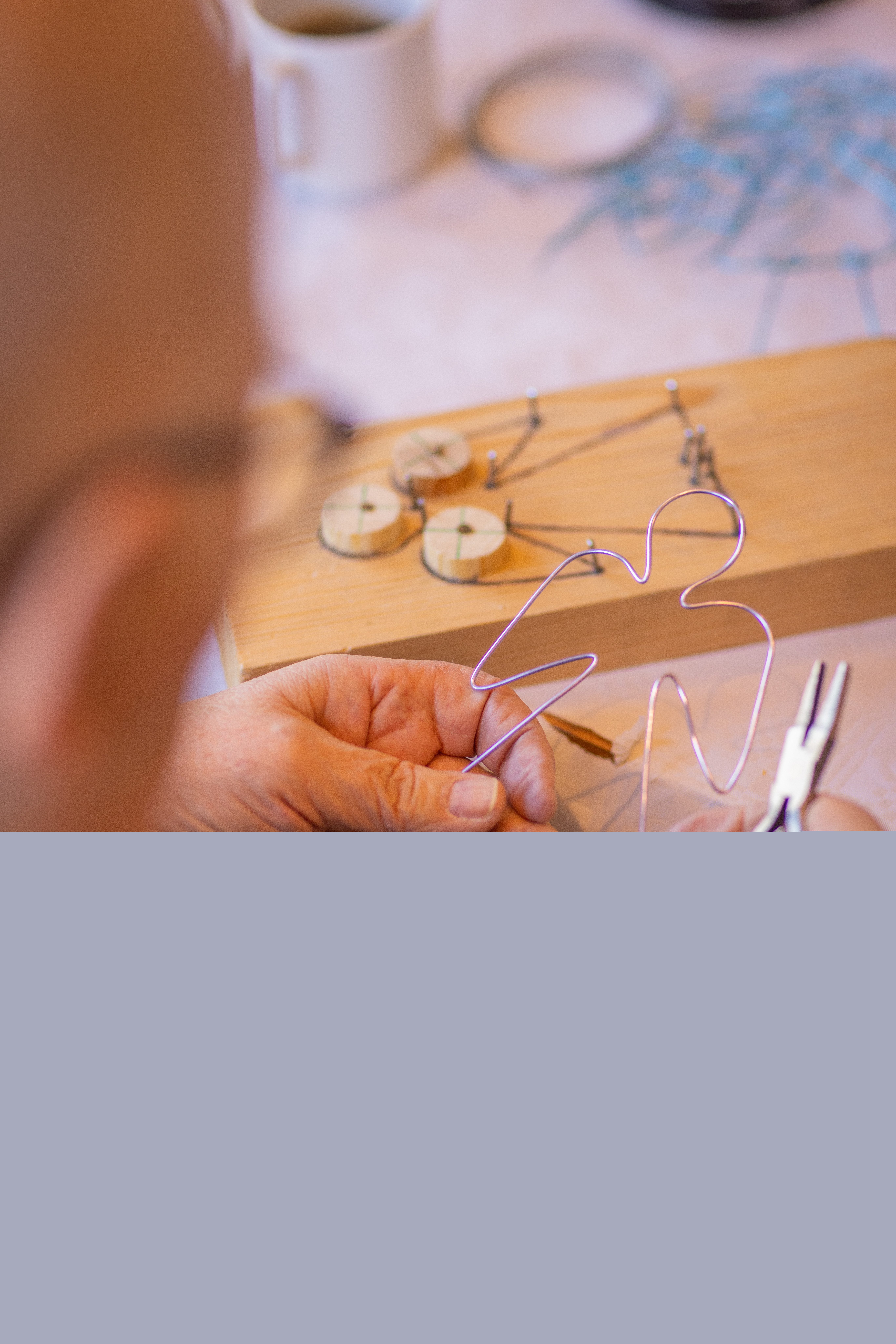 Ett hantverk i trä och ståltråd föreställande en ängel ligger på ett bord. En person i förgrunden håller i en ängel gjord av ståltråd.