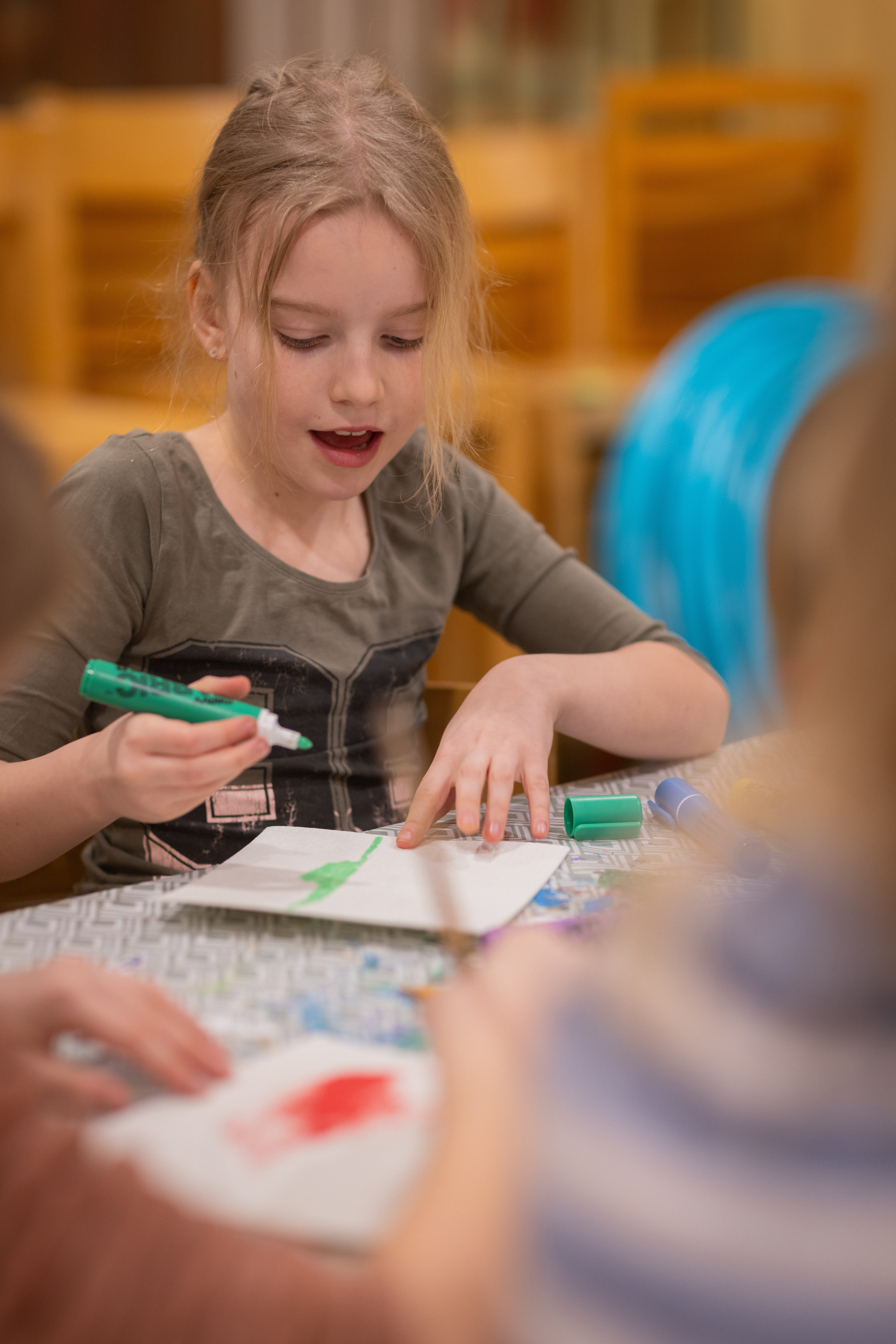 En flicka sitter vid ett bord och ritar med grön tuschpenna.