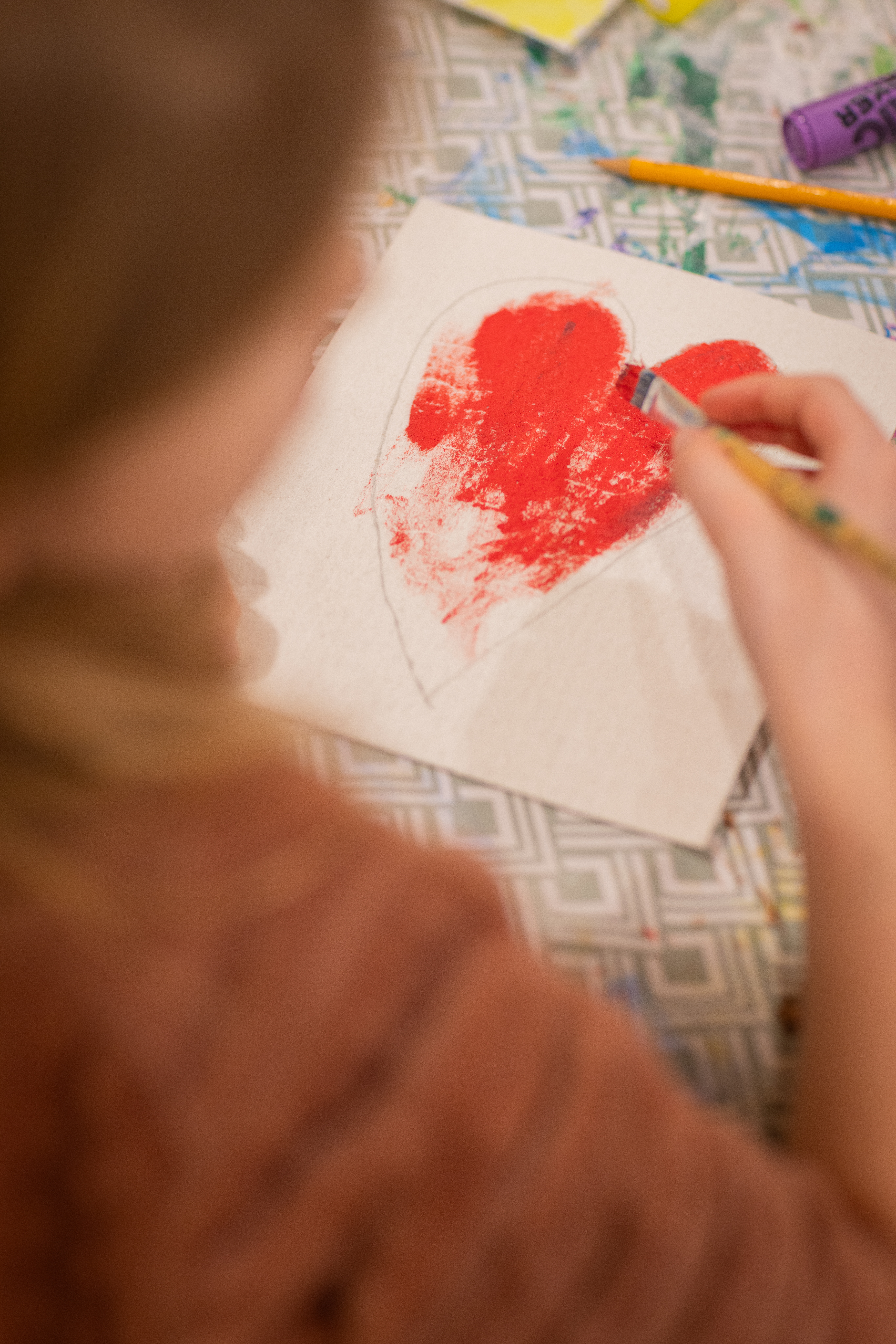 En person sitter vid ett bord och målar ett rött hjärta med målarpensel.