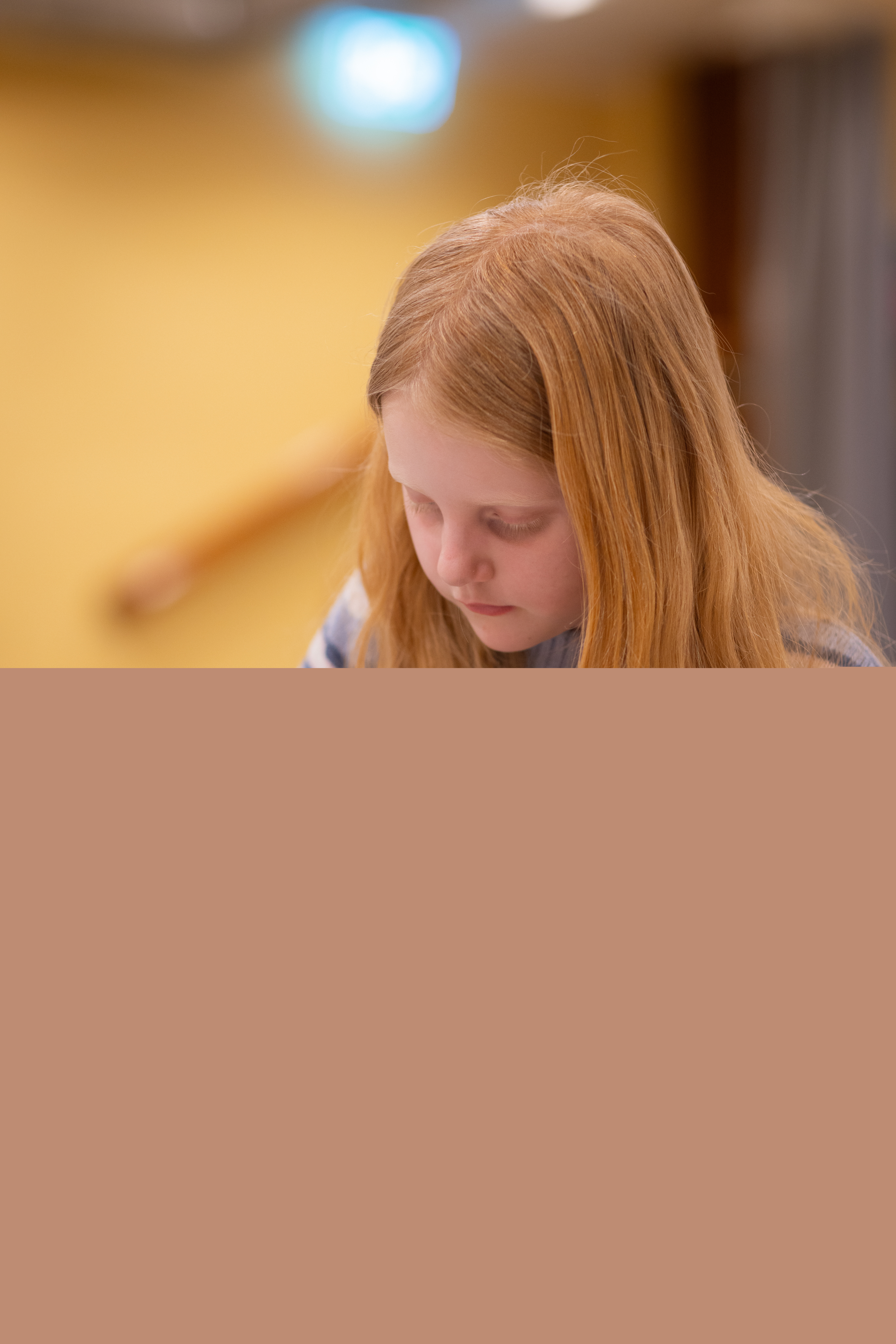 En rödhårig flicka sitter vid ett bord och målar med pensel.