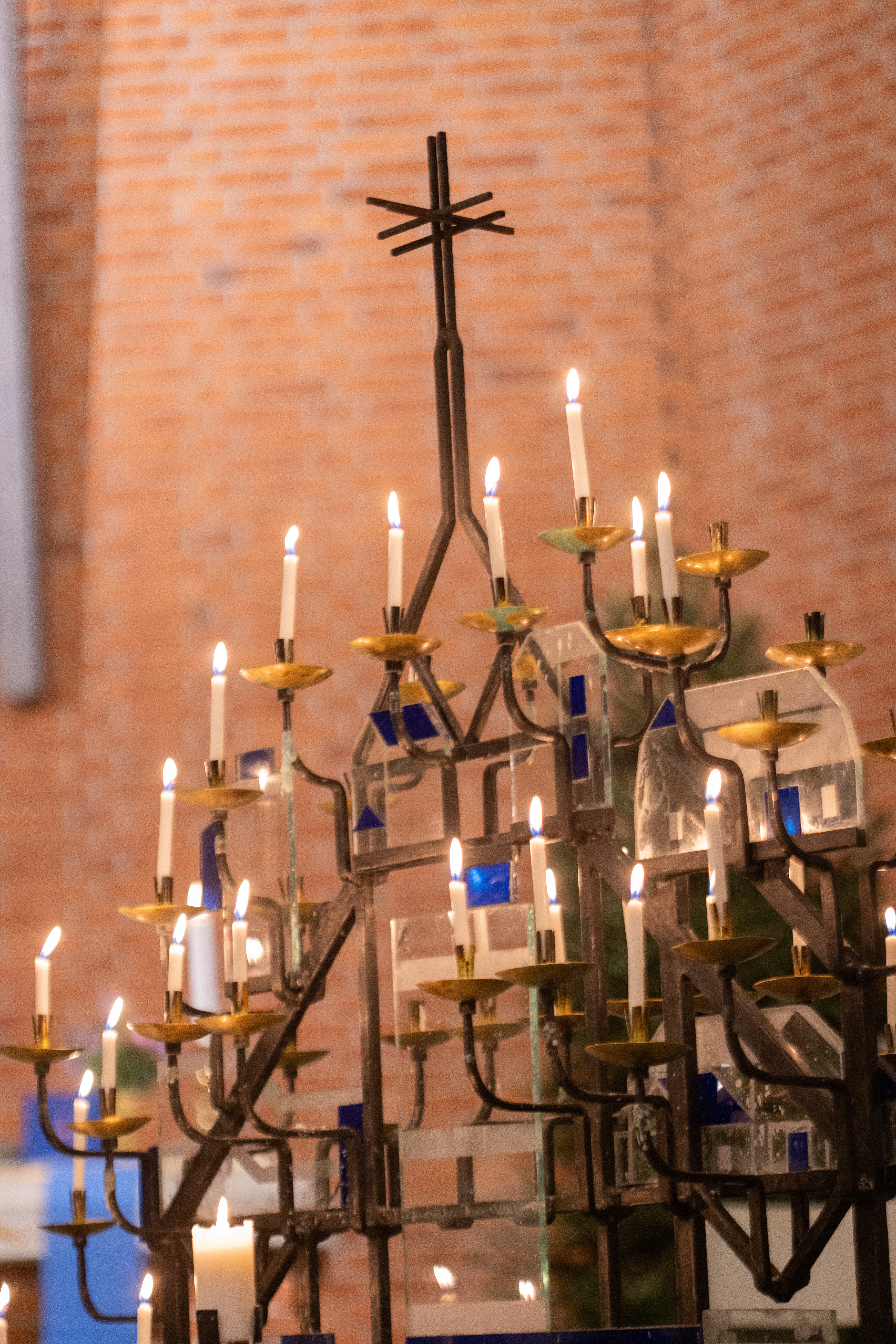 En ljusbärare med många tända ljus i. Rött tegel i bakgrunden.