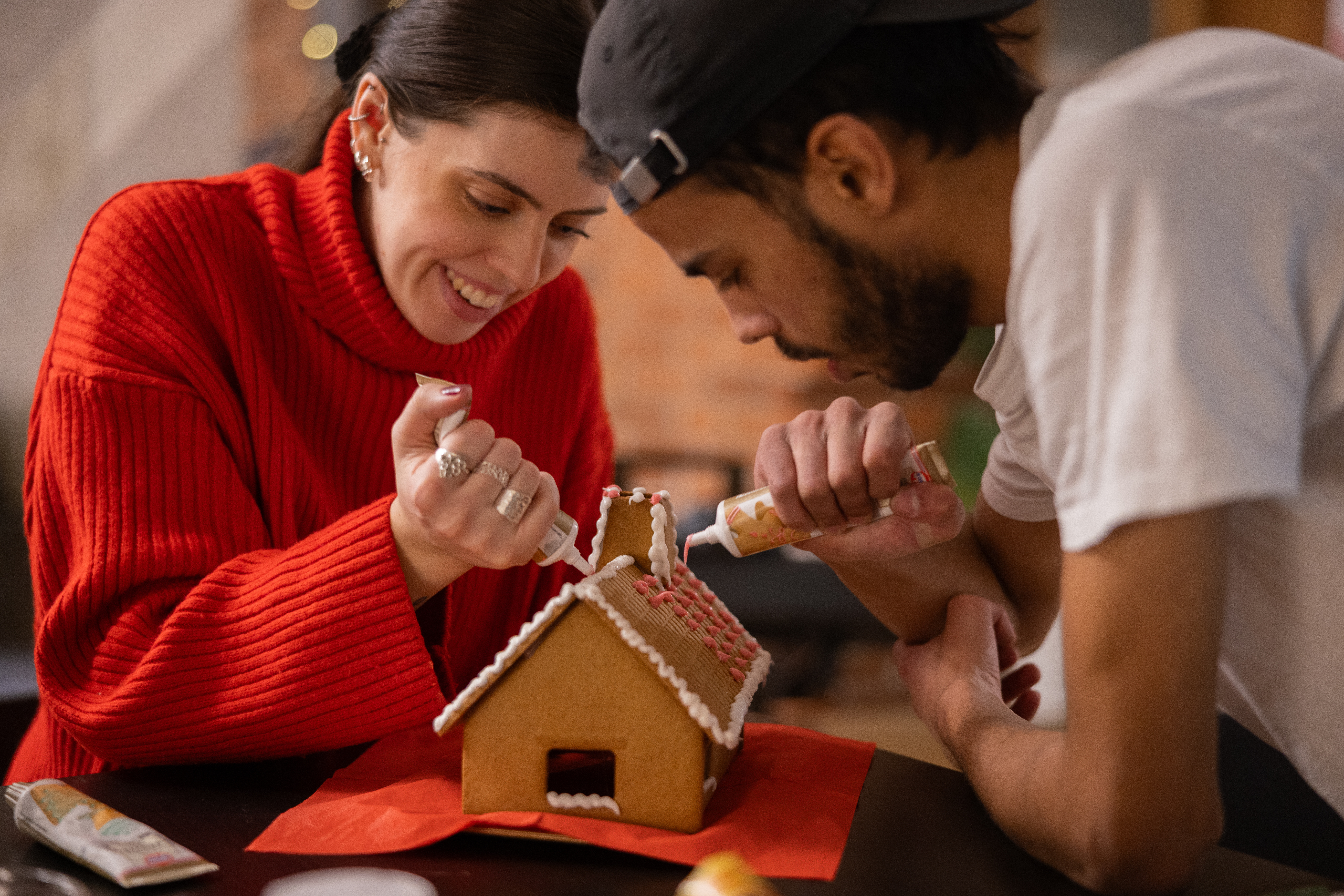 En kvinna och en man dekorerar ett pepparkakshus med glasyr.