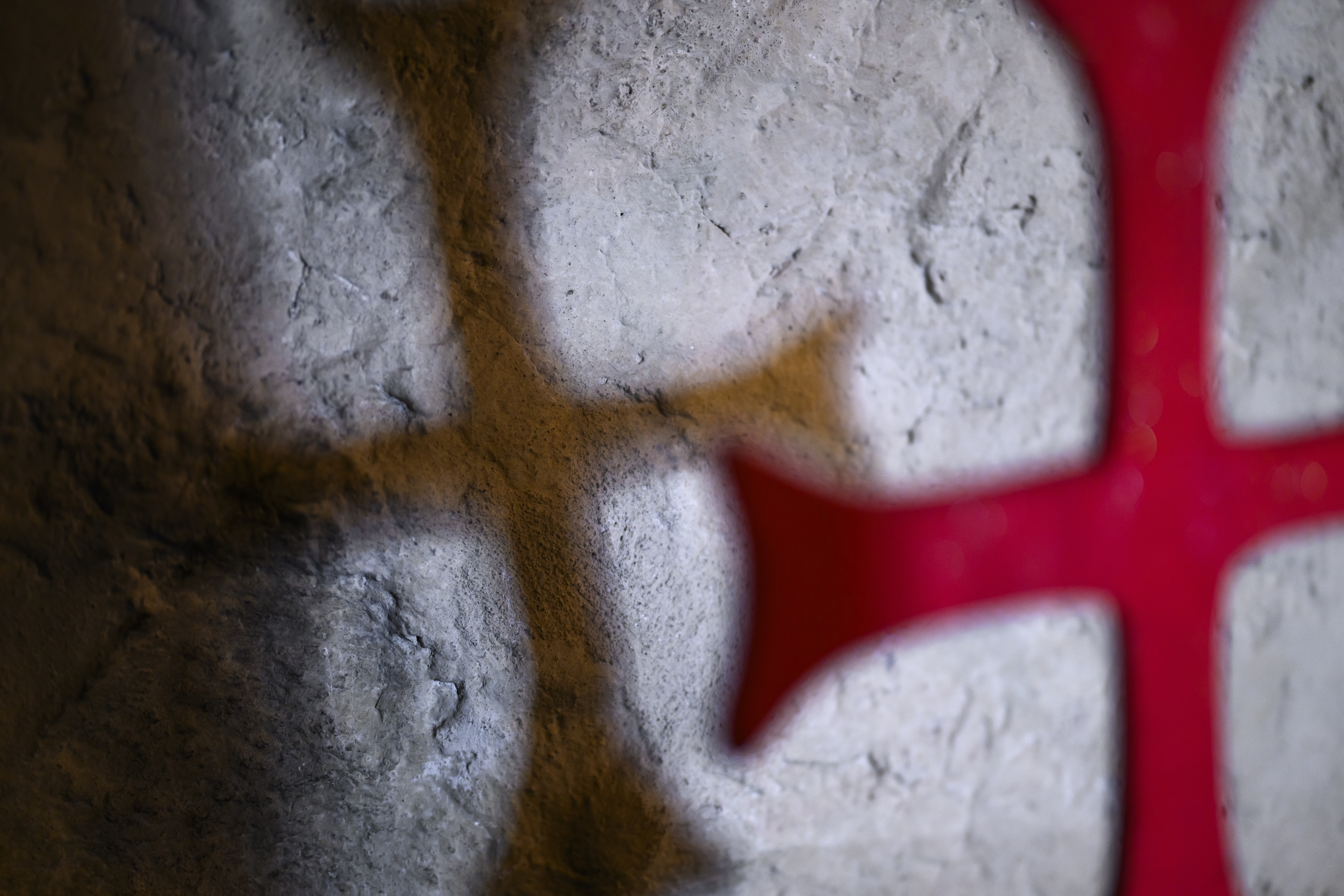 En skugga av ett kors på en stenvägg. Ett rött kors i förgrunden.