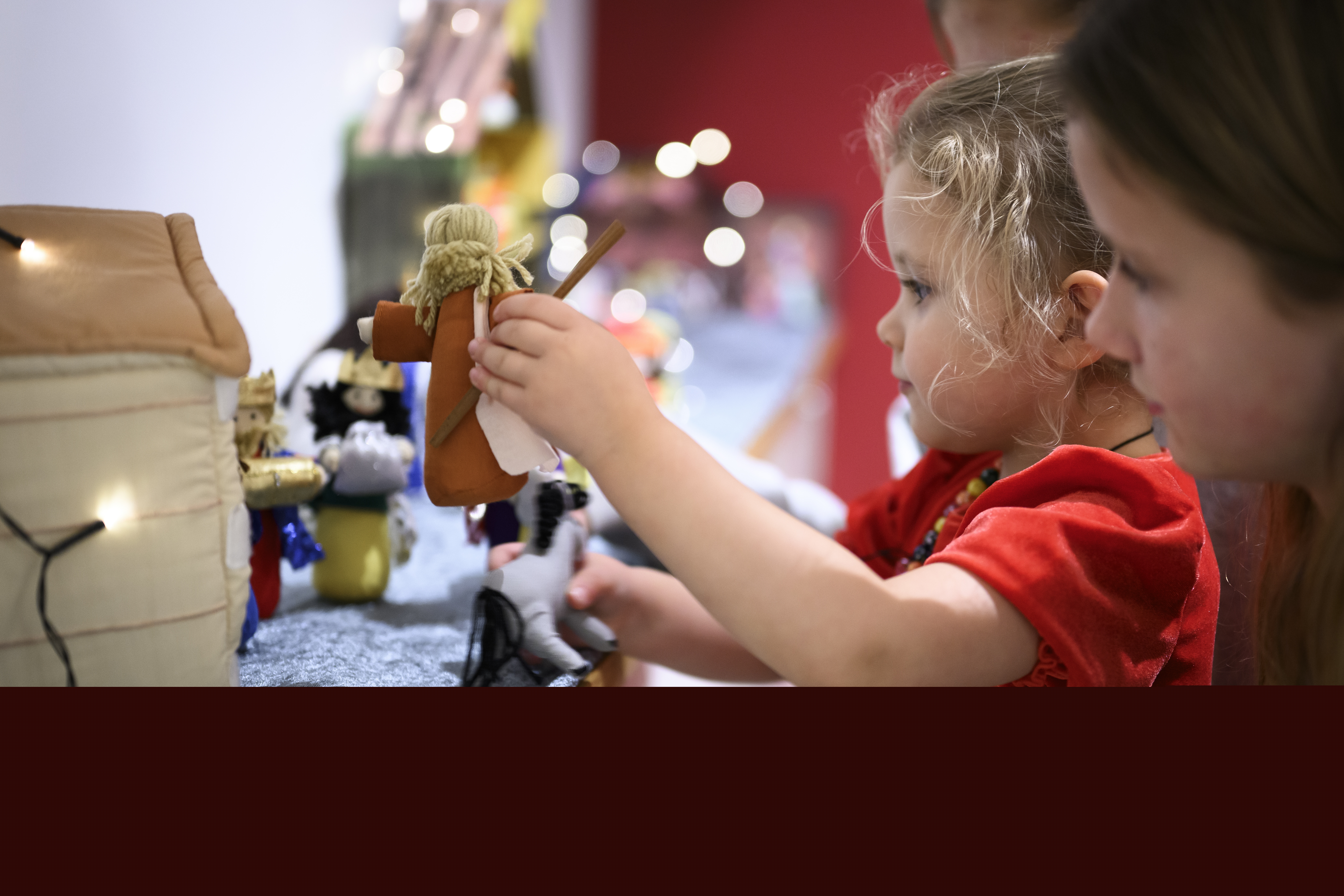 Ett litet barn i röd tröja leker med en julkrubba i mjukistyg.