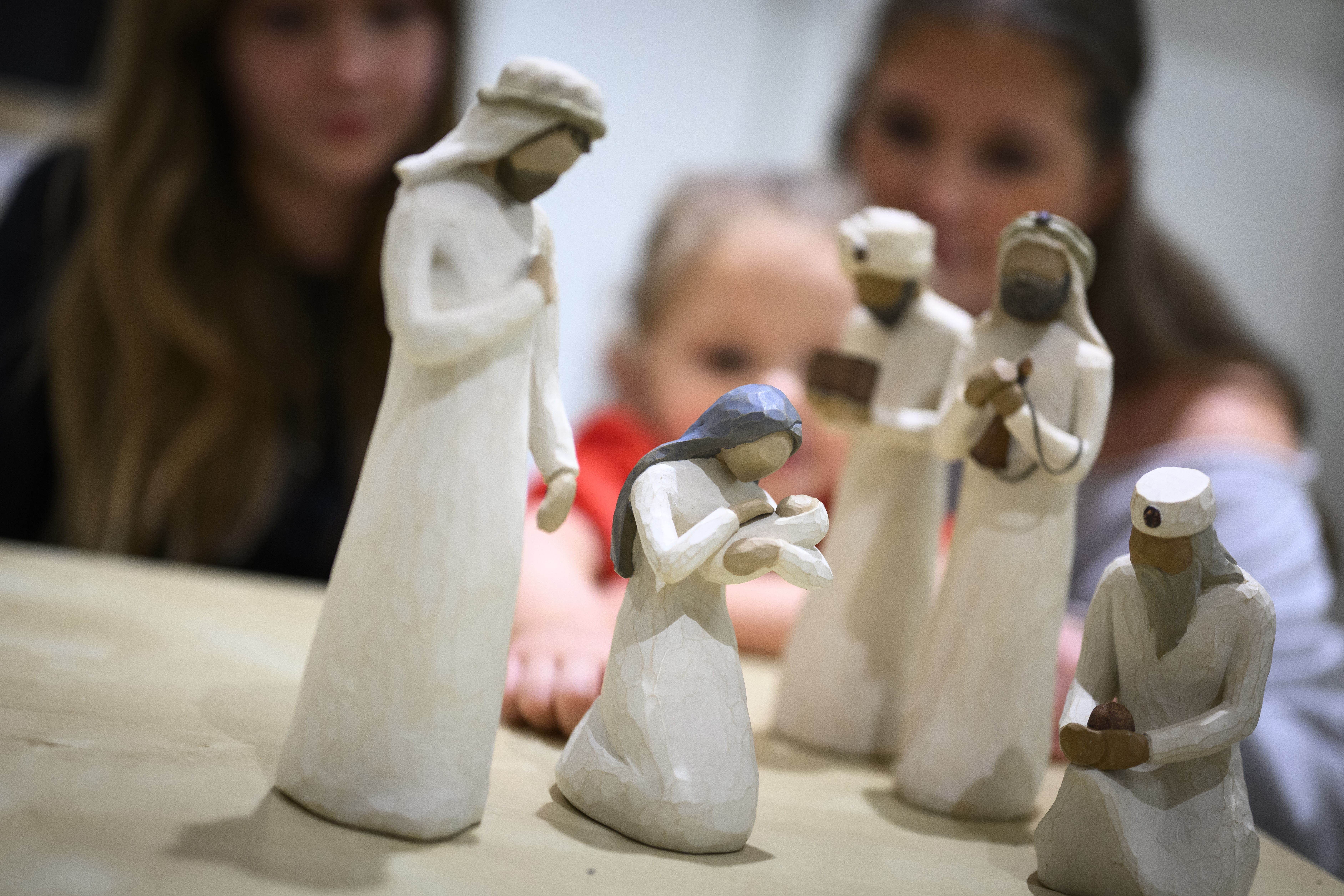 Trädockor som föreställer Jungfru Maria med Jesus-barnet i famnen och de tre vise männen står på ett bord. Ett barn och två ungdomar sitter runt bordet.