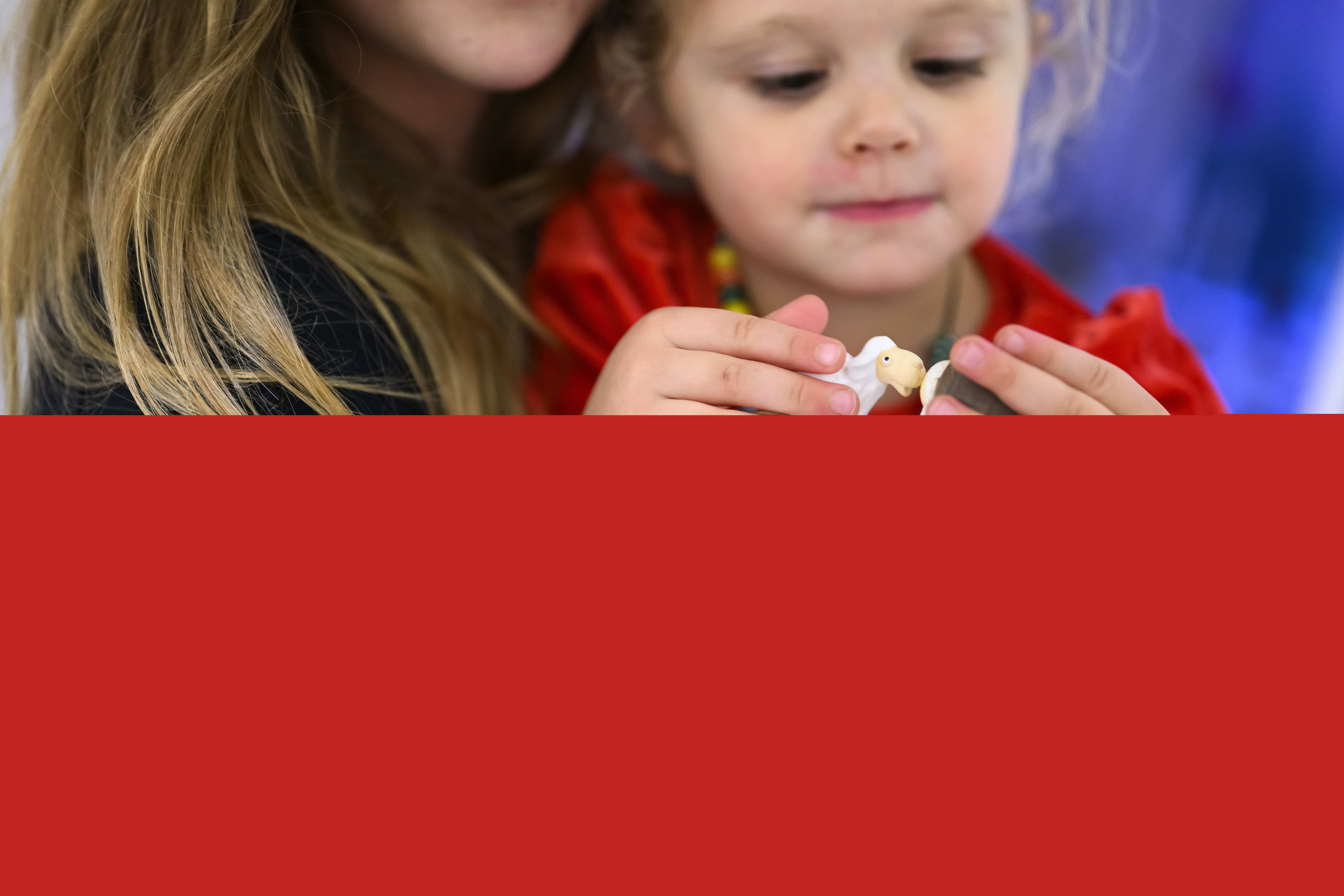 Ett litet barn sitter i famnen på en person. Barnet håller små figurer som föreställer ett vitt får och Jesusbarnet i krubban. Fåret pussar på Jesusbarnet.