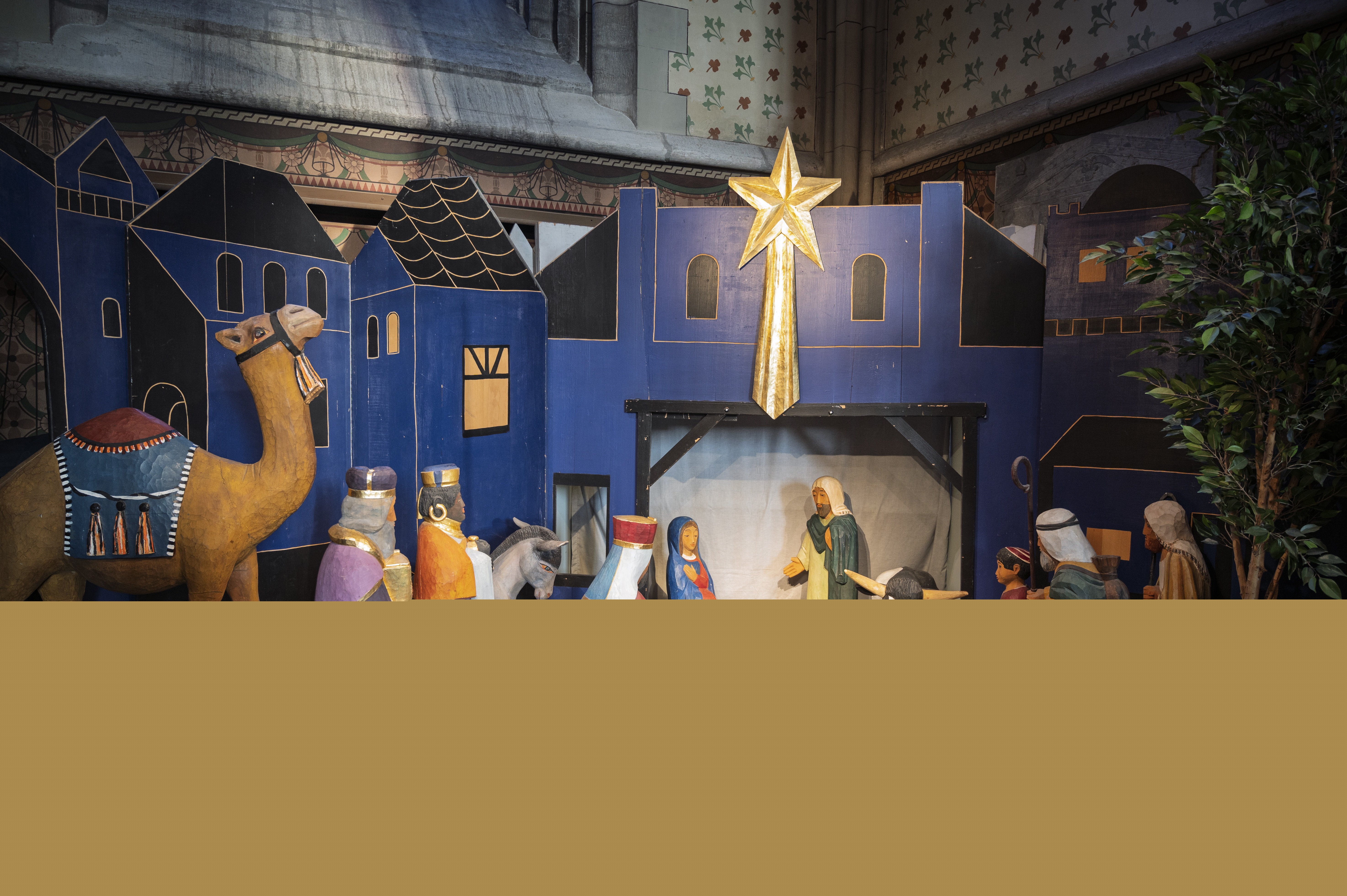 En julkrubba i ett blått hus med en stjärna på. Trädockor som föreställer de tre vise männen och en kamel i förgrunden.