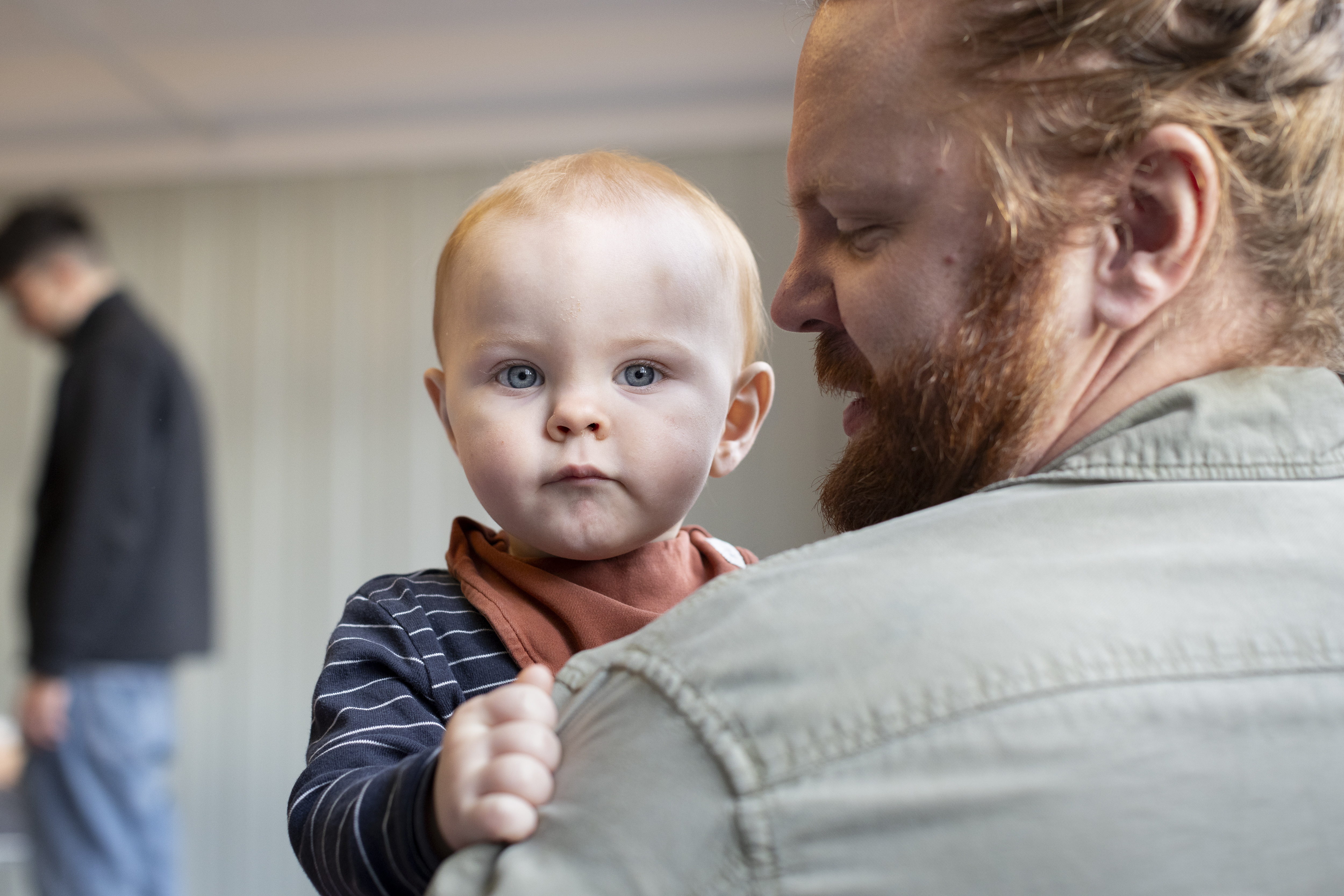 Närbild på ett barn som tittar in i kameran över en mans axel.