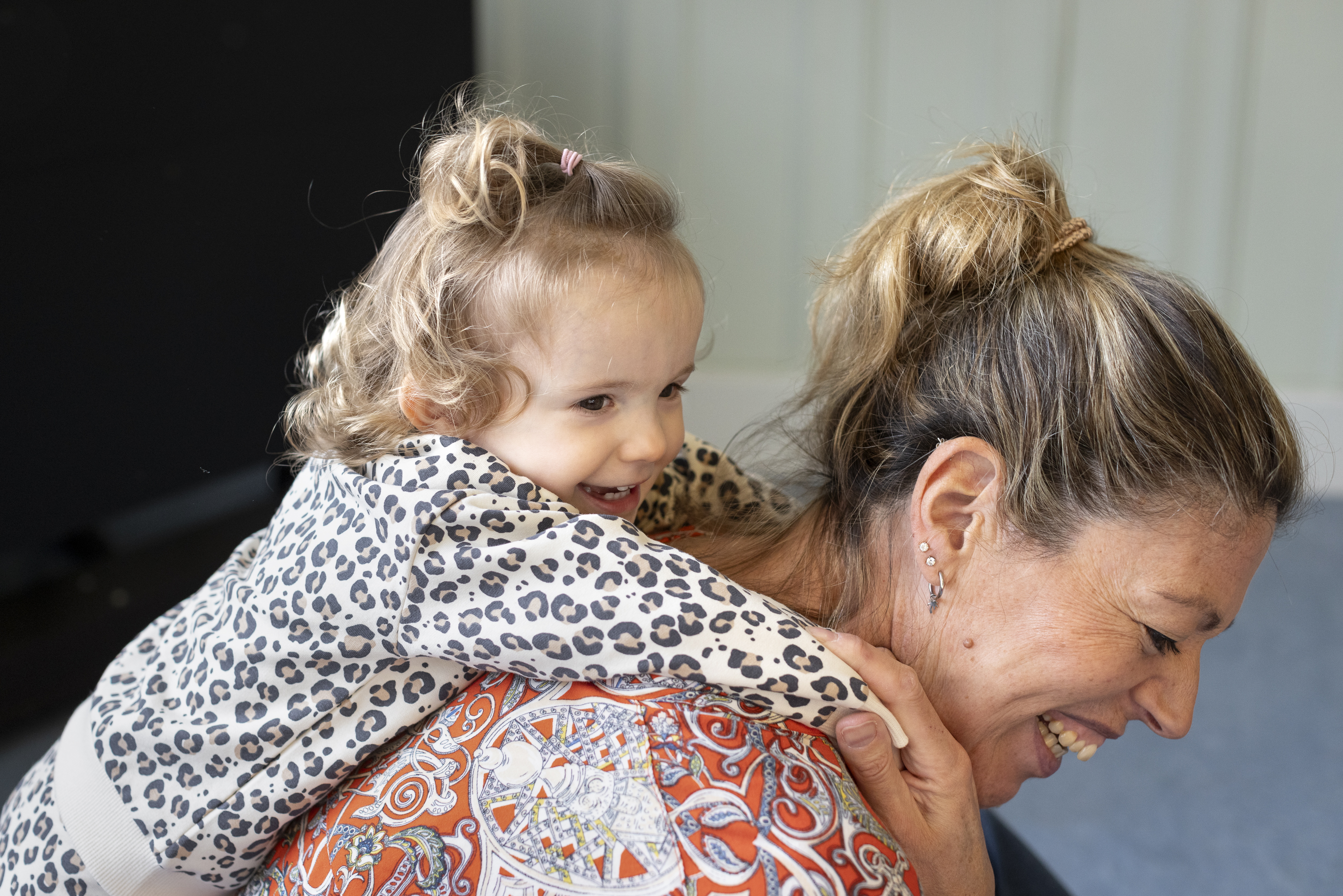 En leende kvinna har ett glatt barn hängandes på ryggen.