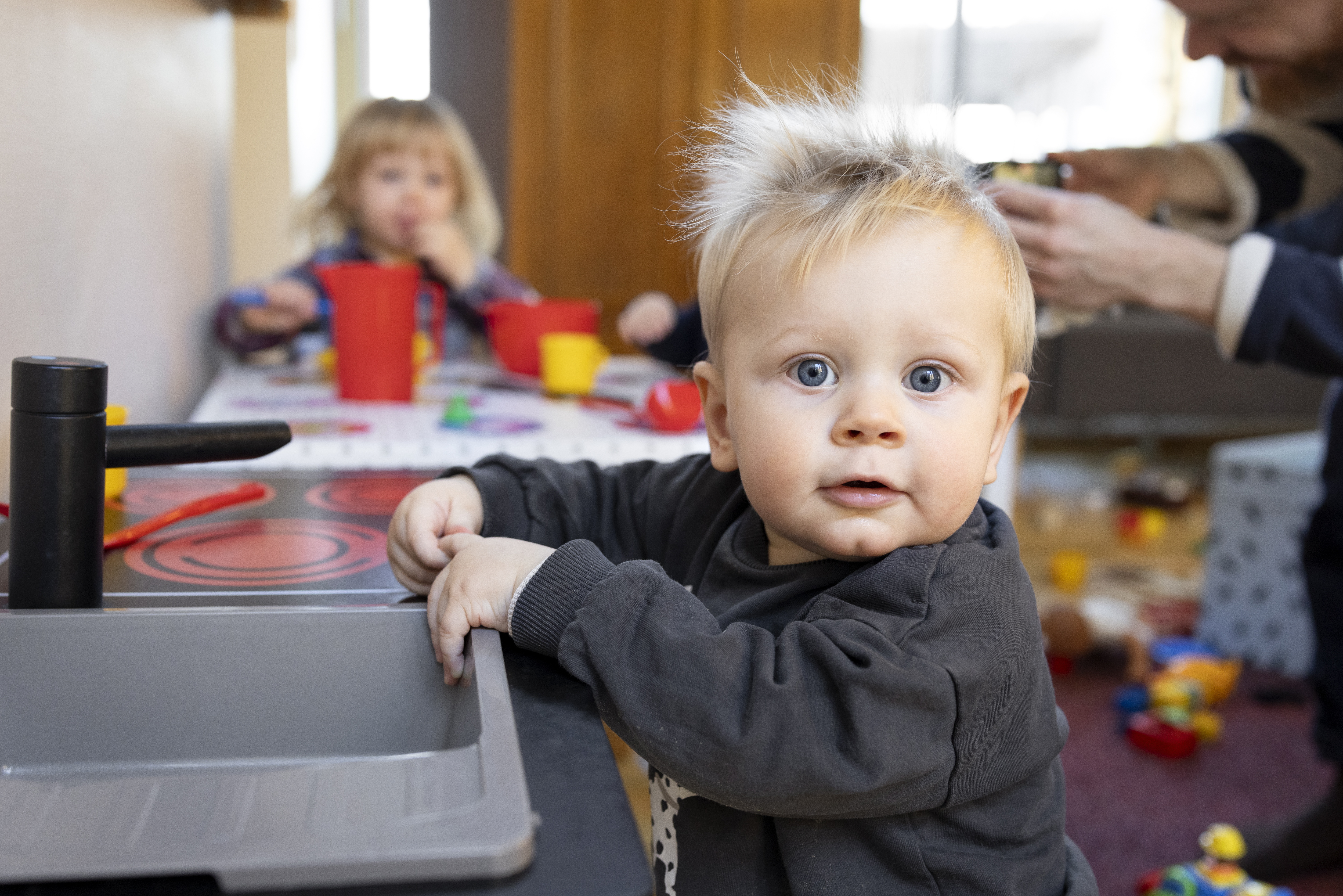 Närbild på ett litet barn som står vid en mini-diskbänk och tittar in i kameran.