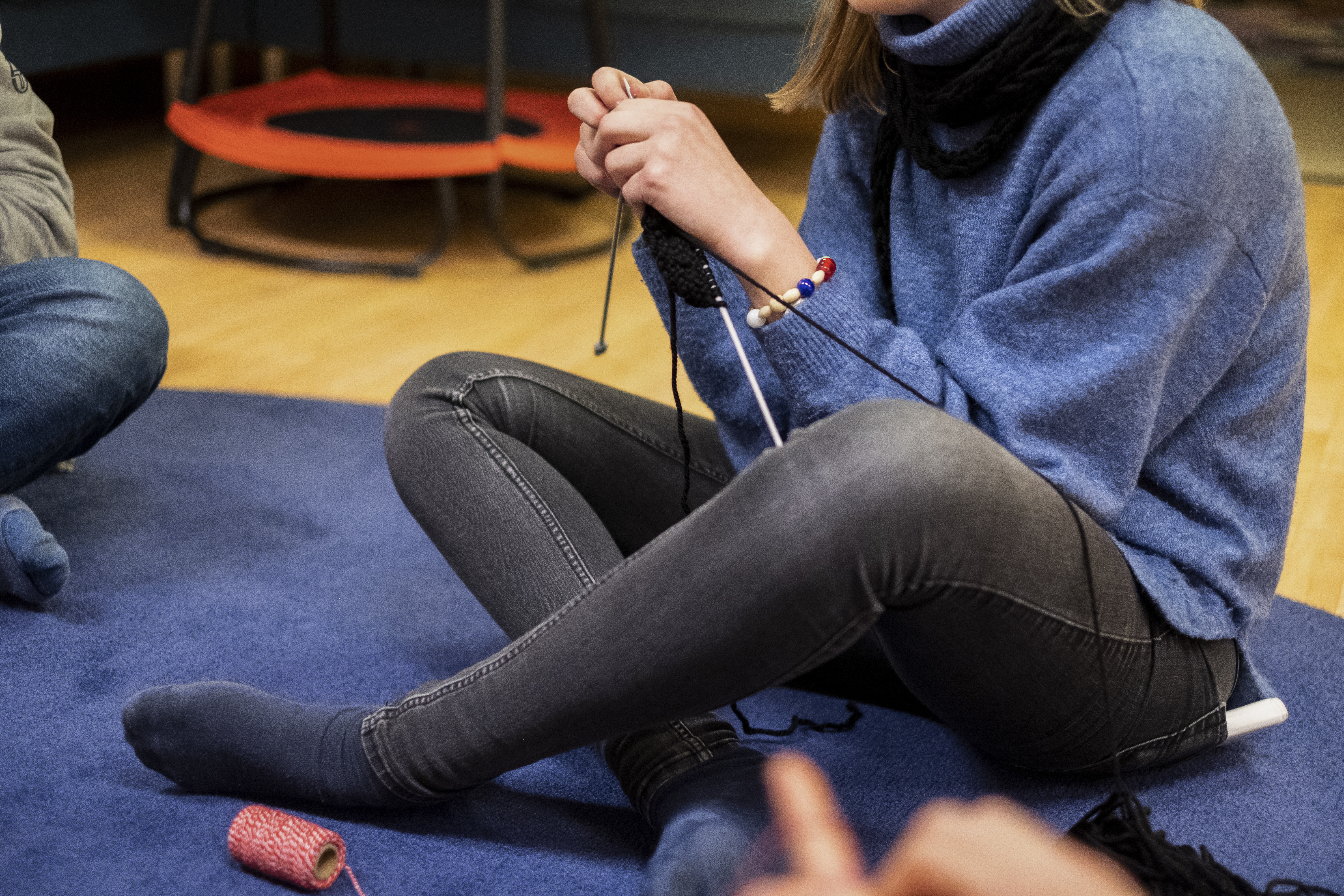 En person sitter på golvet och stickar, med frälsarkransen runt vänster handled.