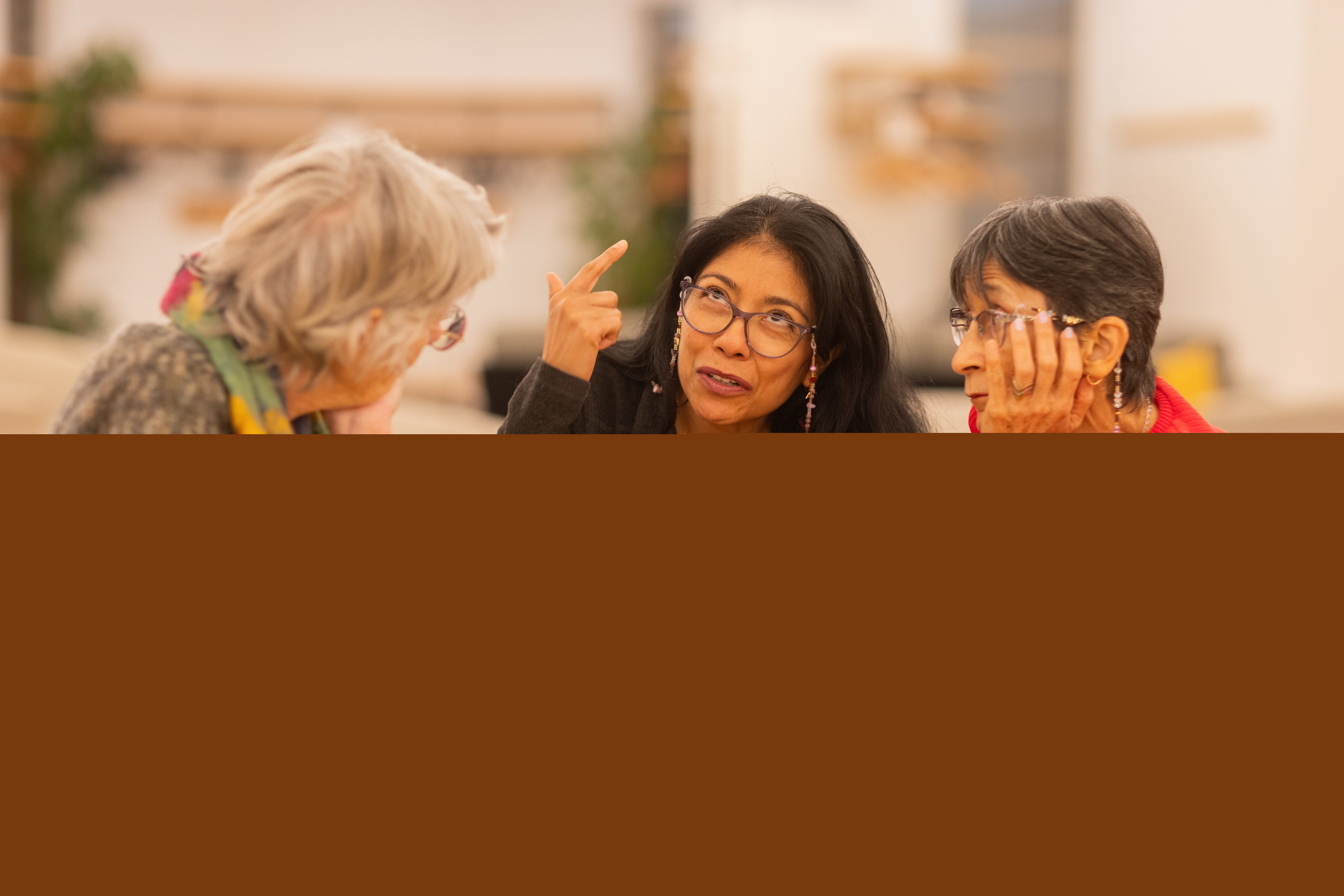 Tre kvinnor sitter vid ett runt bord och samtalar med varandra.