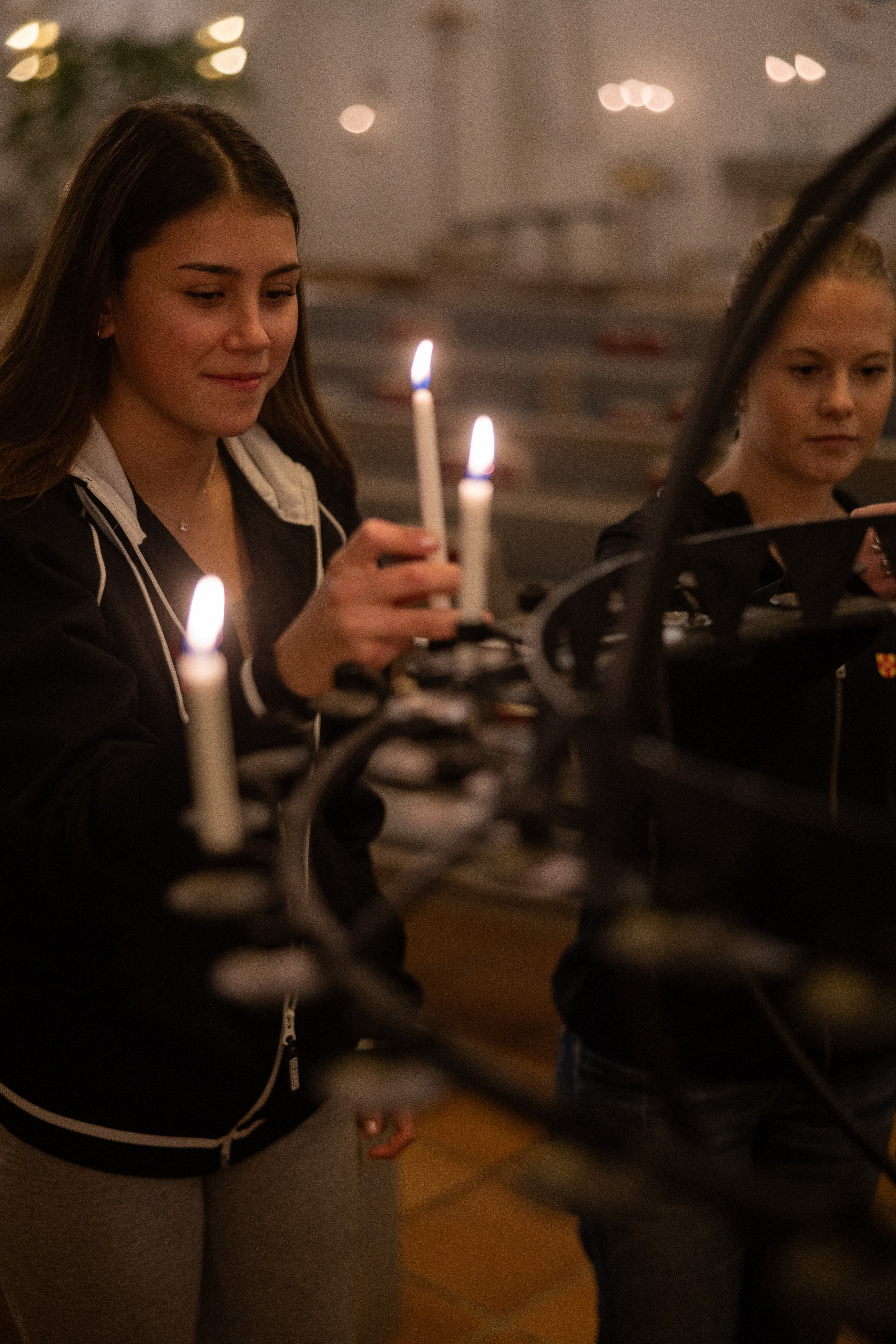 Två unga tjejer står framför en ljusbärare. En av kvinnorna sätter ner ett tänt ljus.