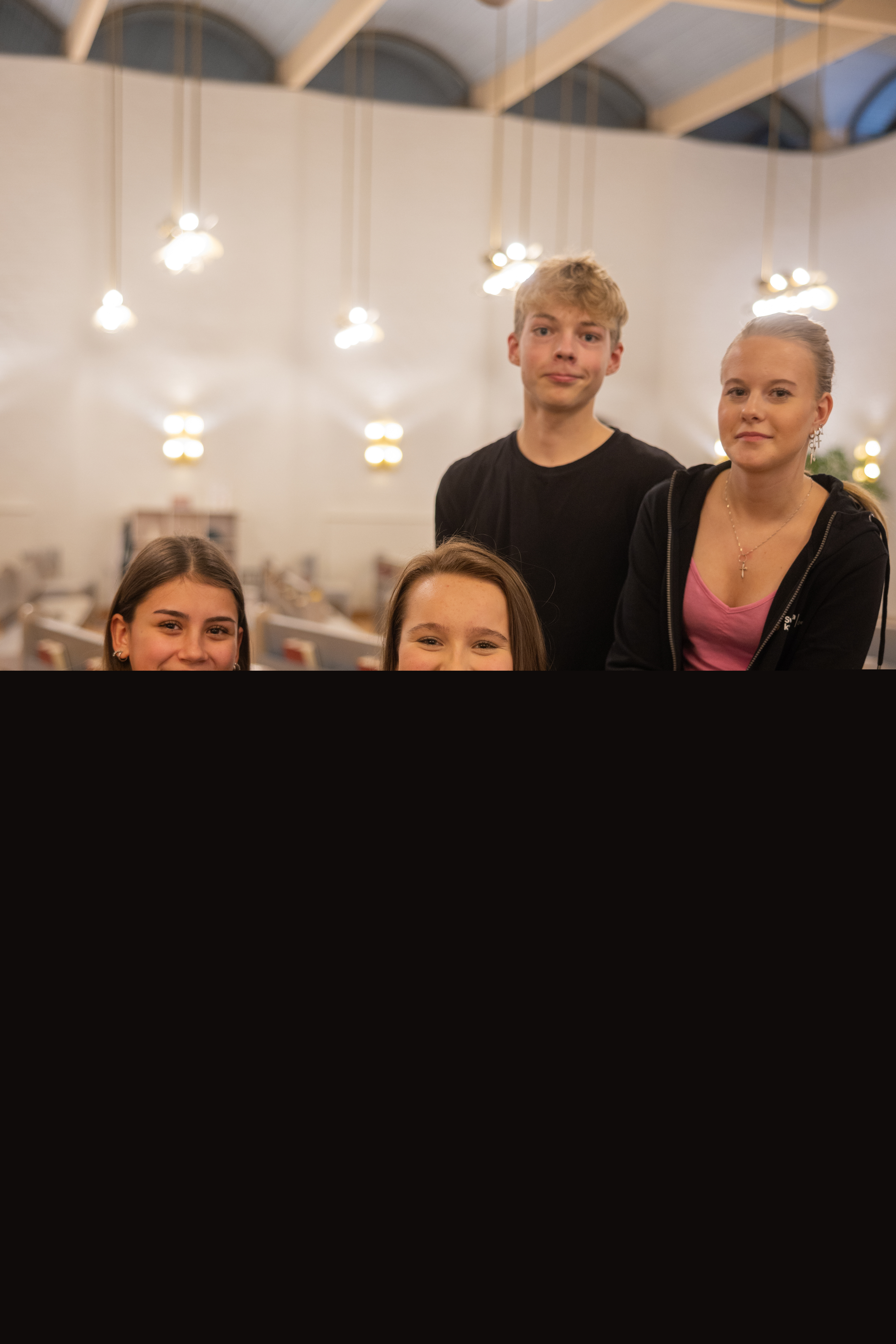 Fyra glada ungdomar sitter i kyrkbänken och tittar in i kameran.